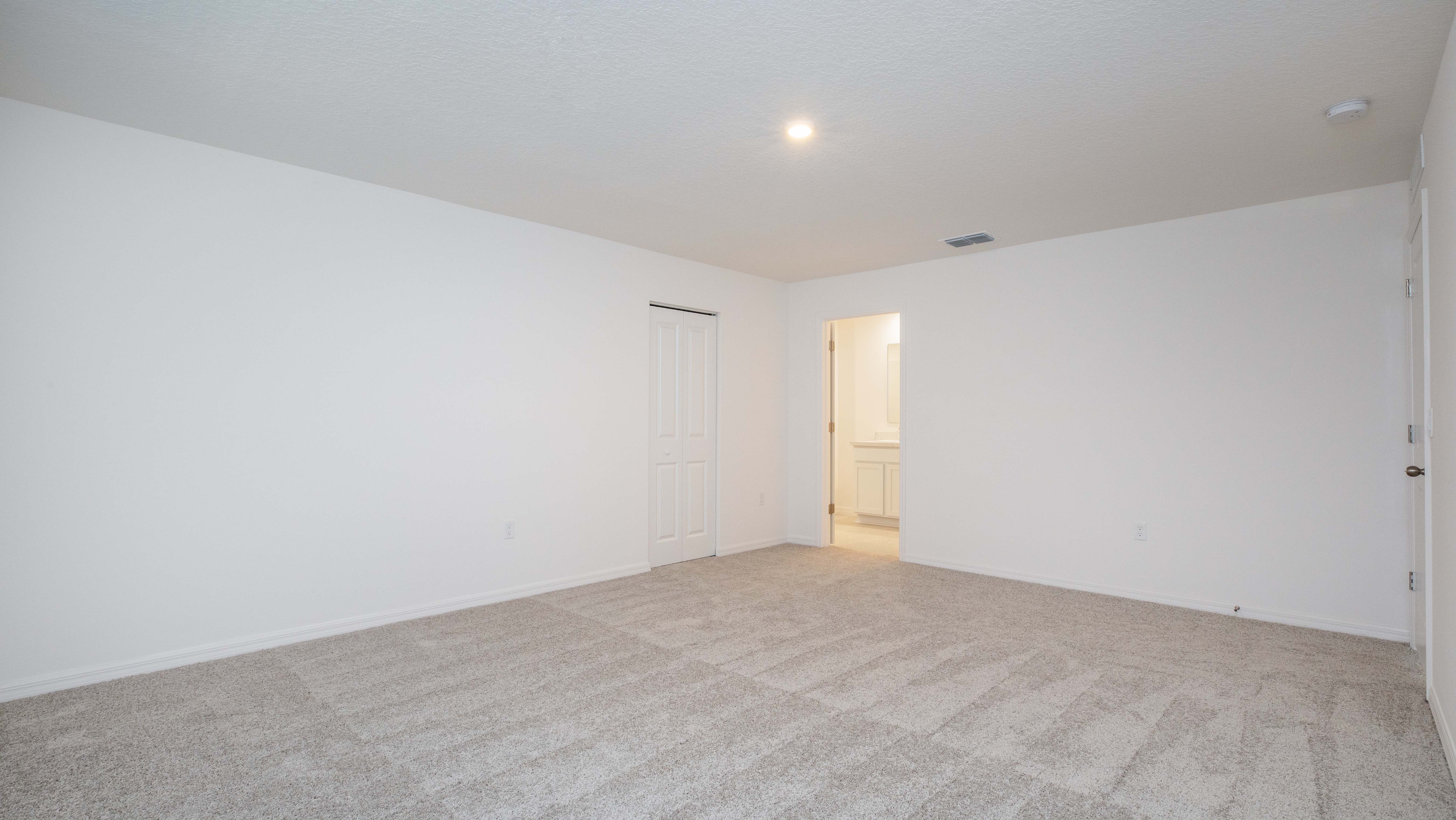 Empty carpeted room with a closed closet door and an open door leading to a lit adjoining space.