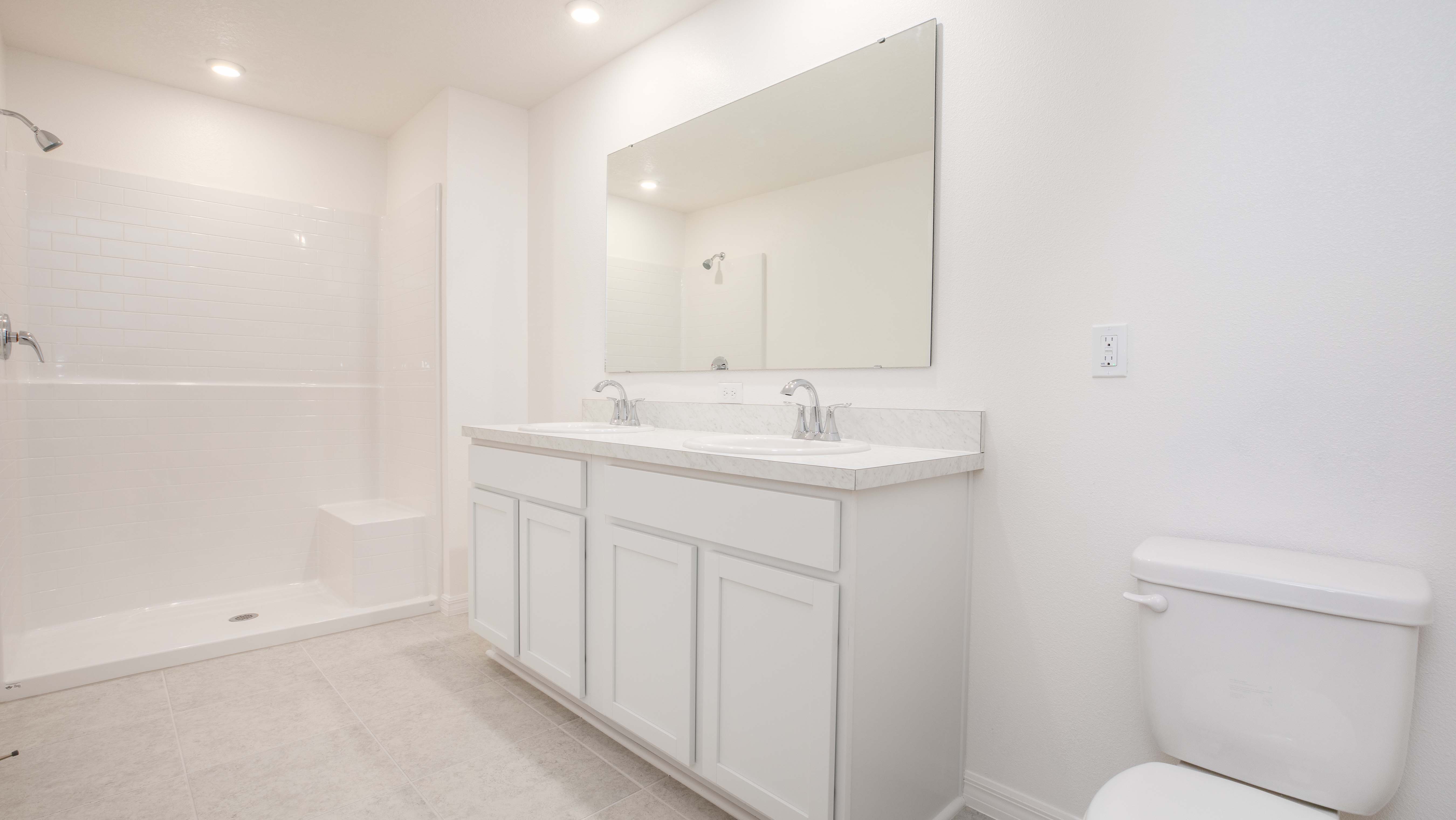 Modern white bathroom featuring a spacious walk-in shower, double sink vanity, large mirror, and a toilet.