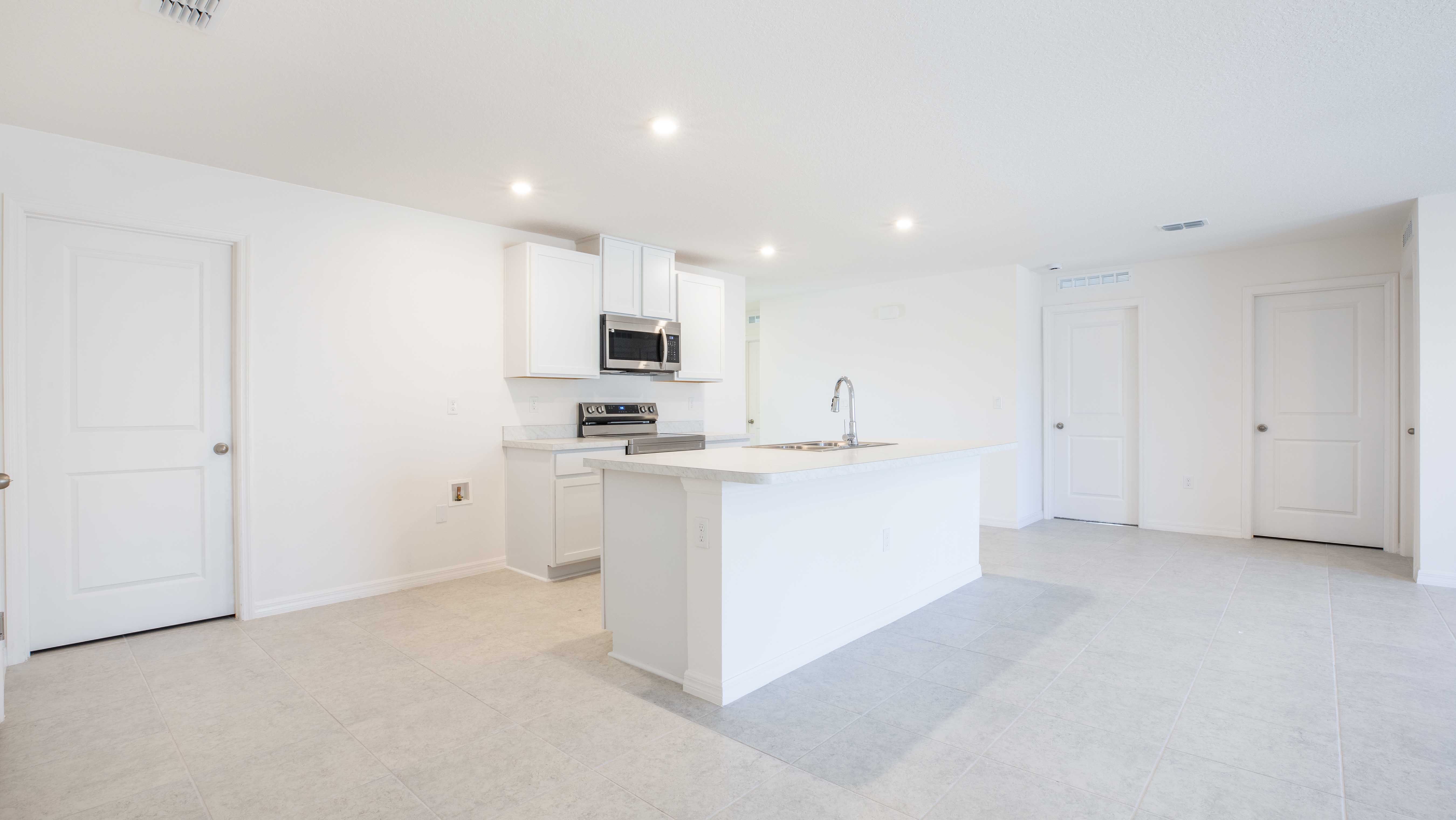 Modern kitchen with white cabinets, island with sink, and stainless steel appliances in an open-plan setting.