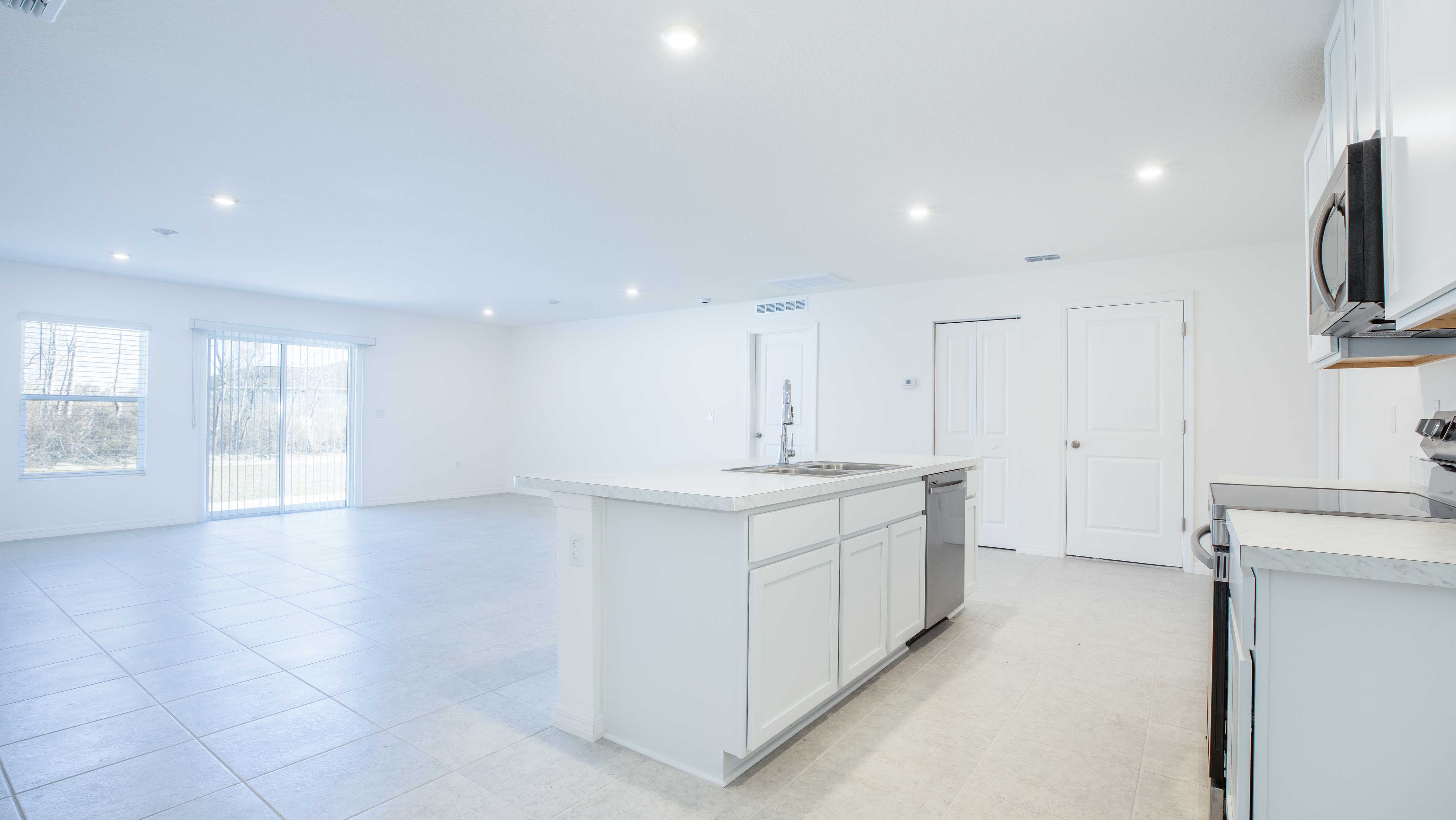 Modern, spacious open-concept kitchen and living area with white cabinetry, large island, and natural light from sliding glass doors.