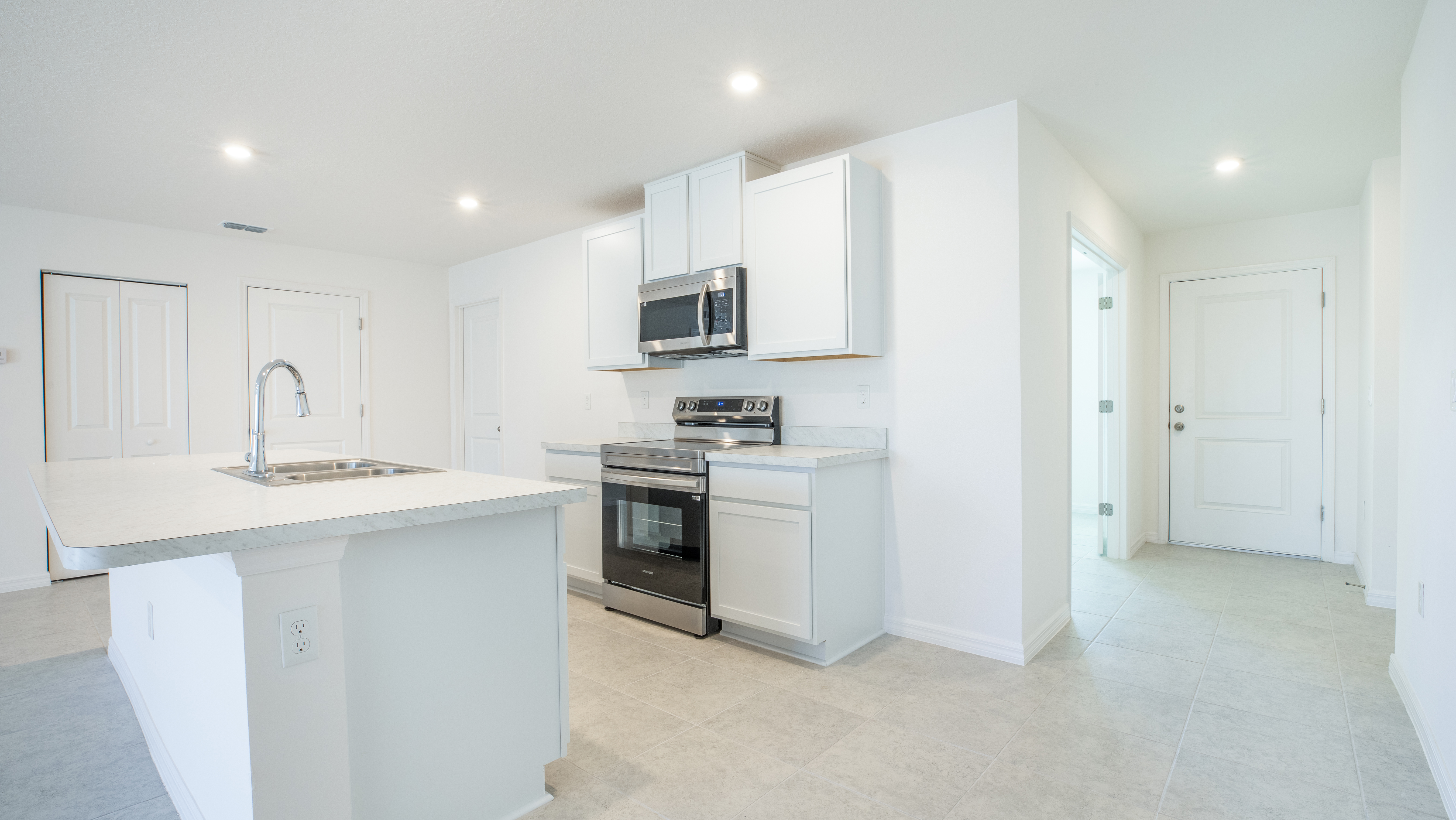 Modern kitchen with white cabinets, stainless steel appliances, and a marble island countertop under recessed lighting.