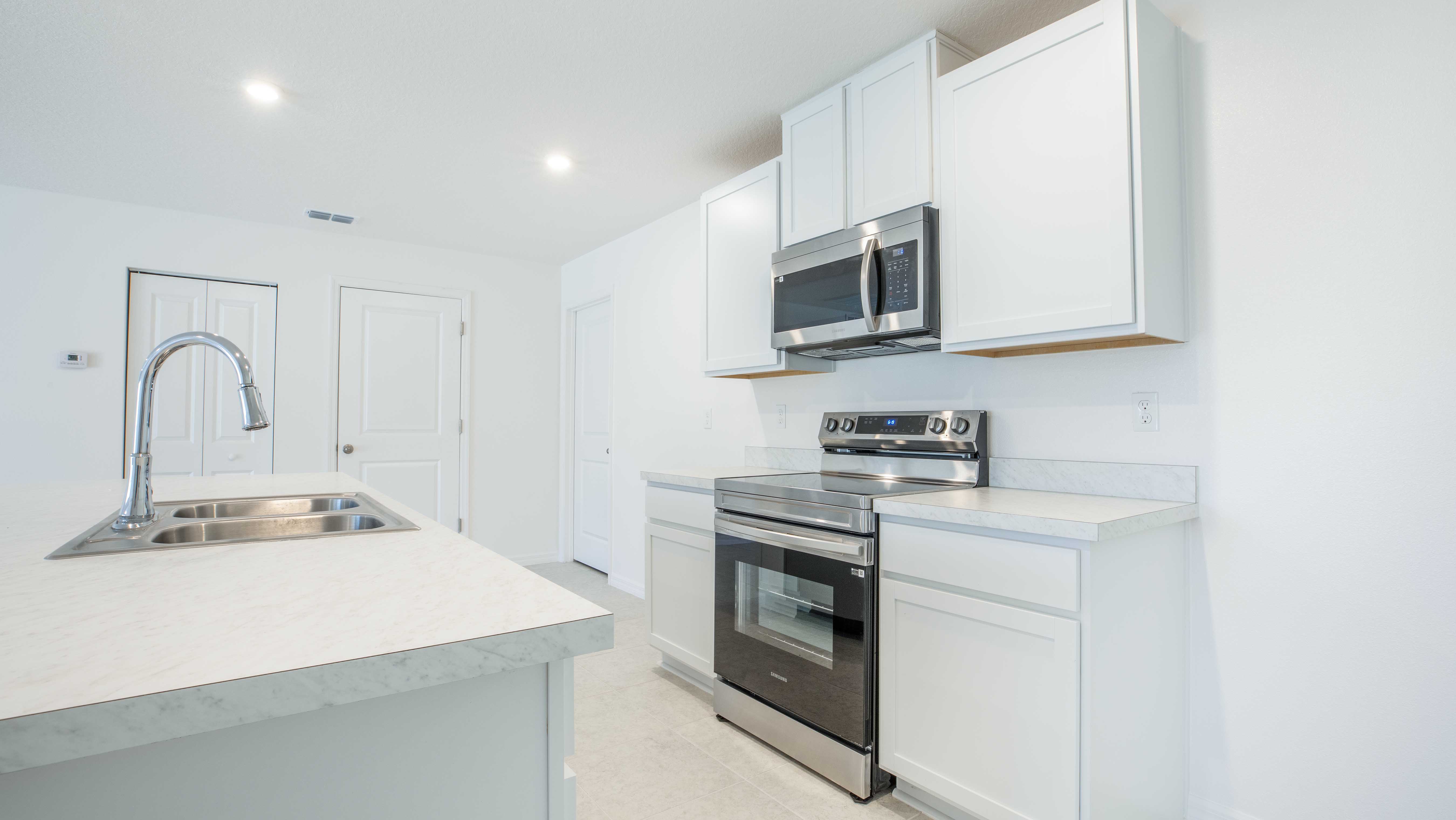Sleek modern kitchen with stainless steel appliances, white cabinets, and a marble countertop island featuring a dual-basin sink.