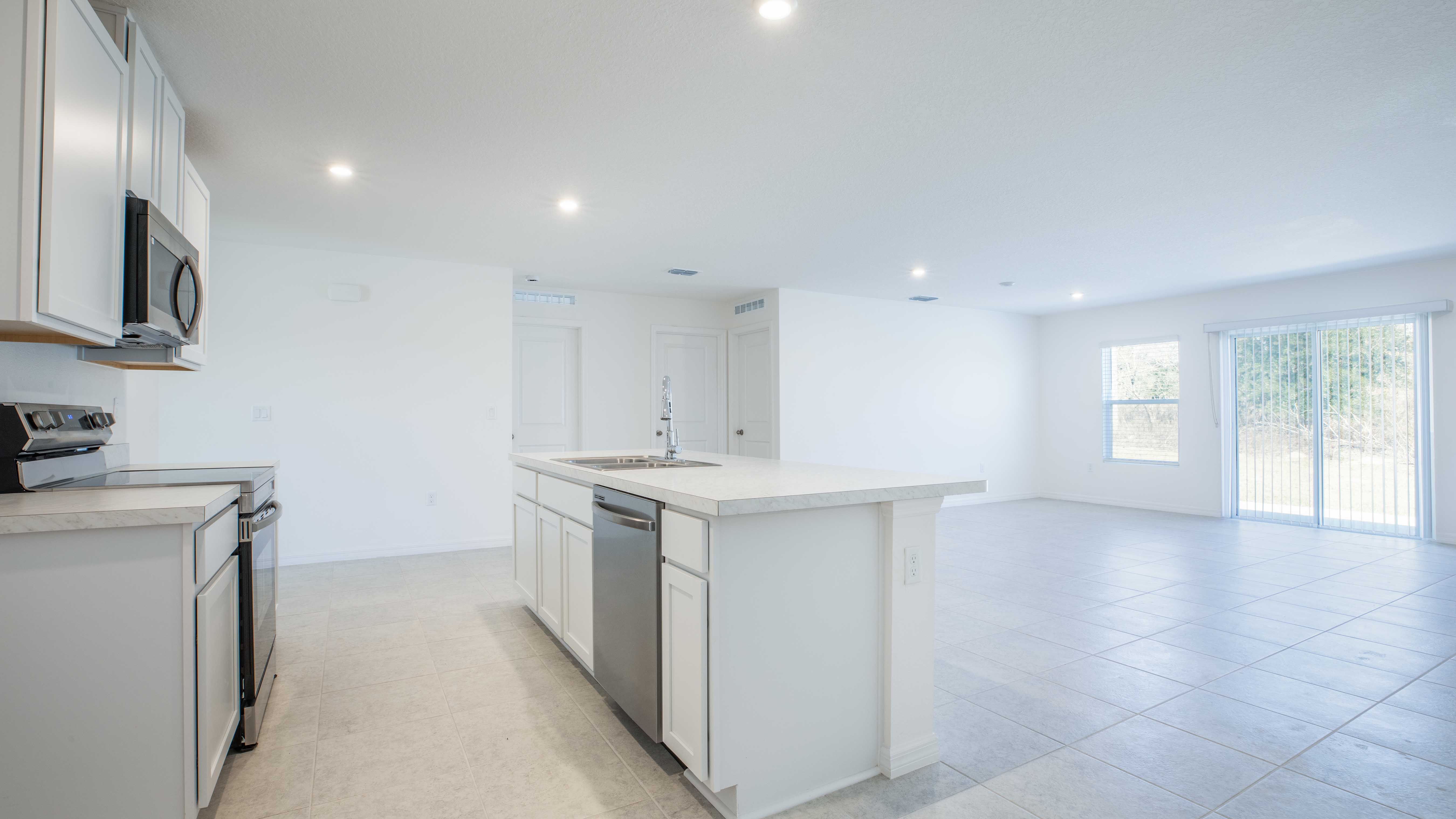 Modern open-concept kitchen with white cabinets, stainless steel appliances, and a spacious island overlooking a bright living room.