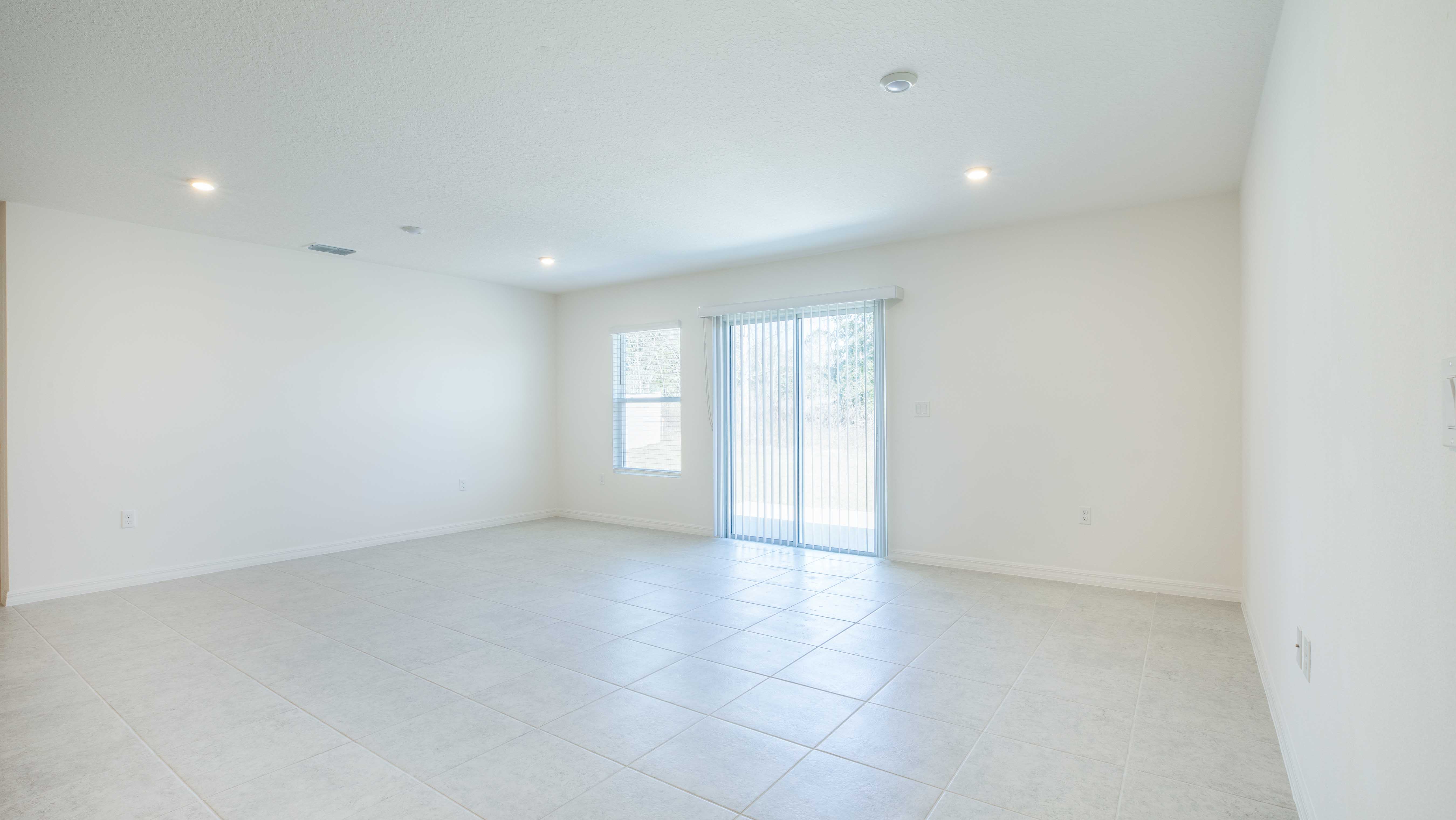 Empty bright room with tiled floor, white walls, and large sliding glass doors leading to a garden.