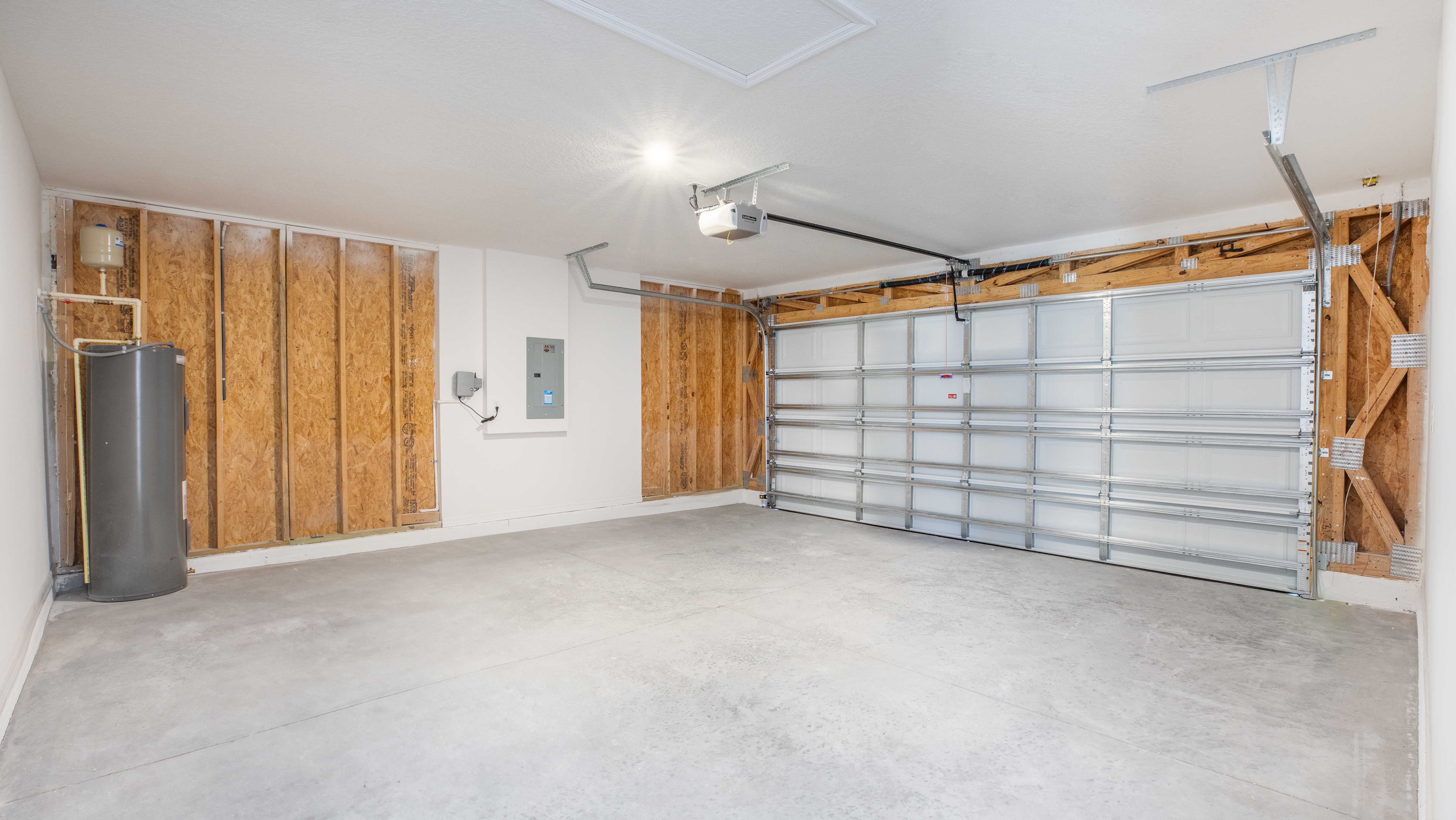 Empty residential garage interior with a water heater, electrical panels, and a closed double garage door.
