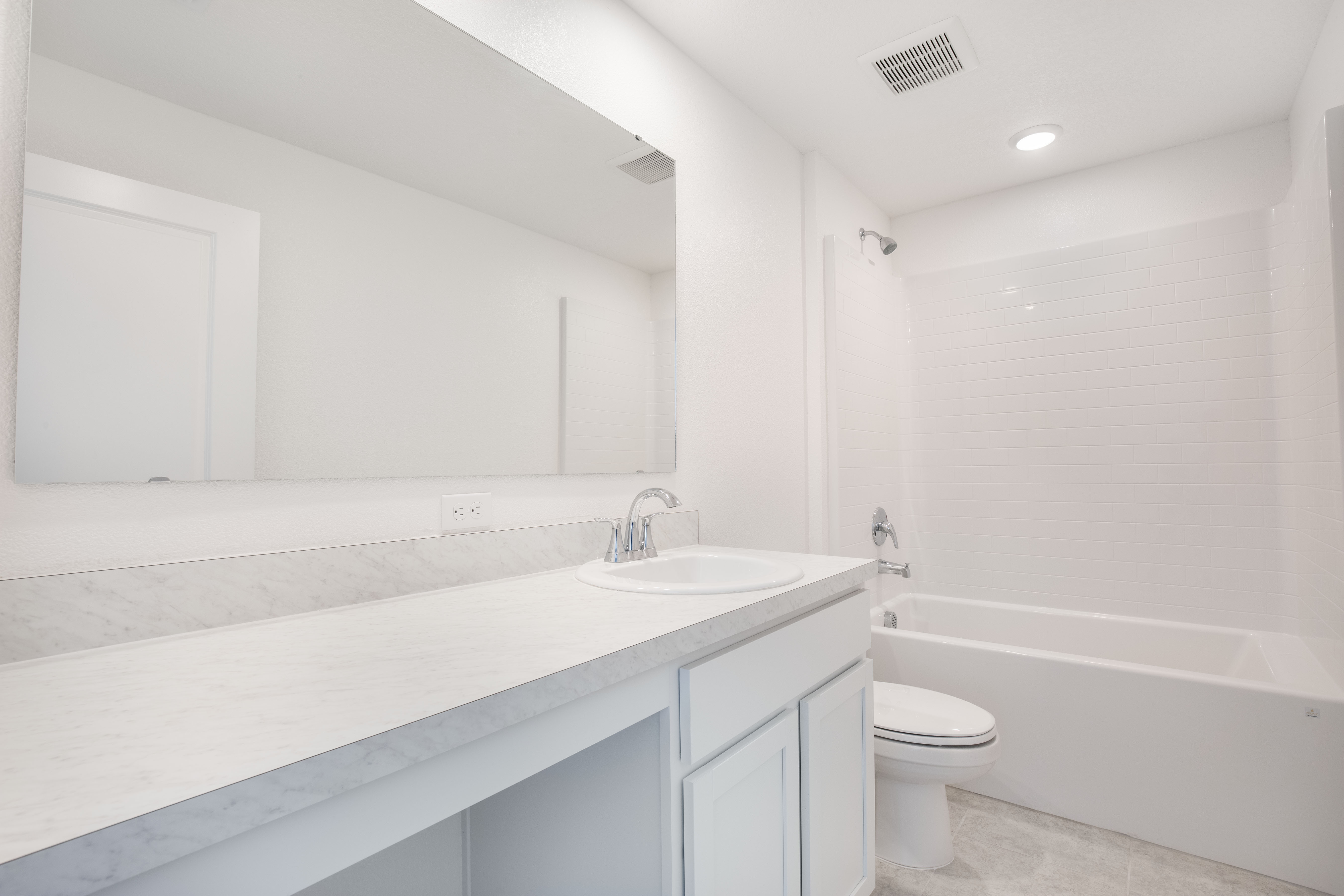 Minimalist white bathroom with a marble countertop, large mirror, and a tiled shower-bathtub combo.