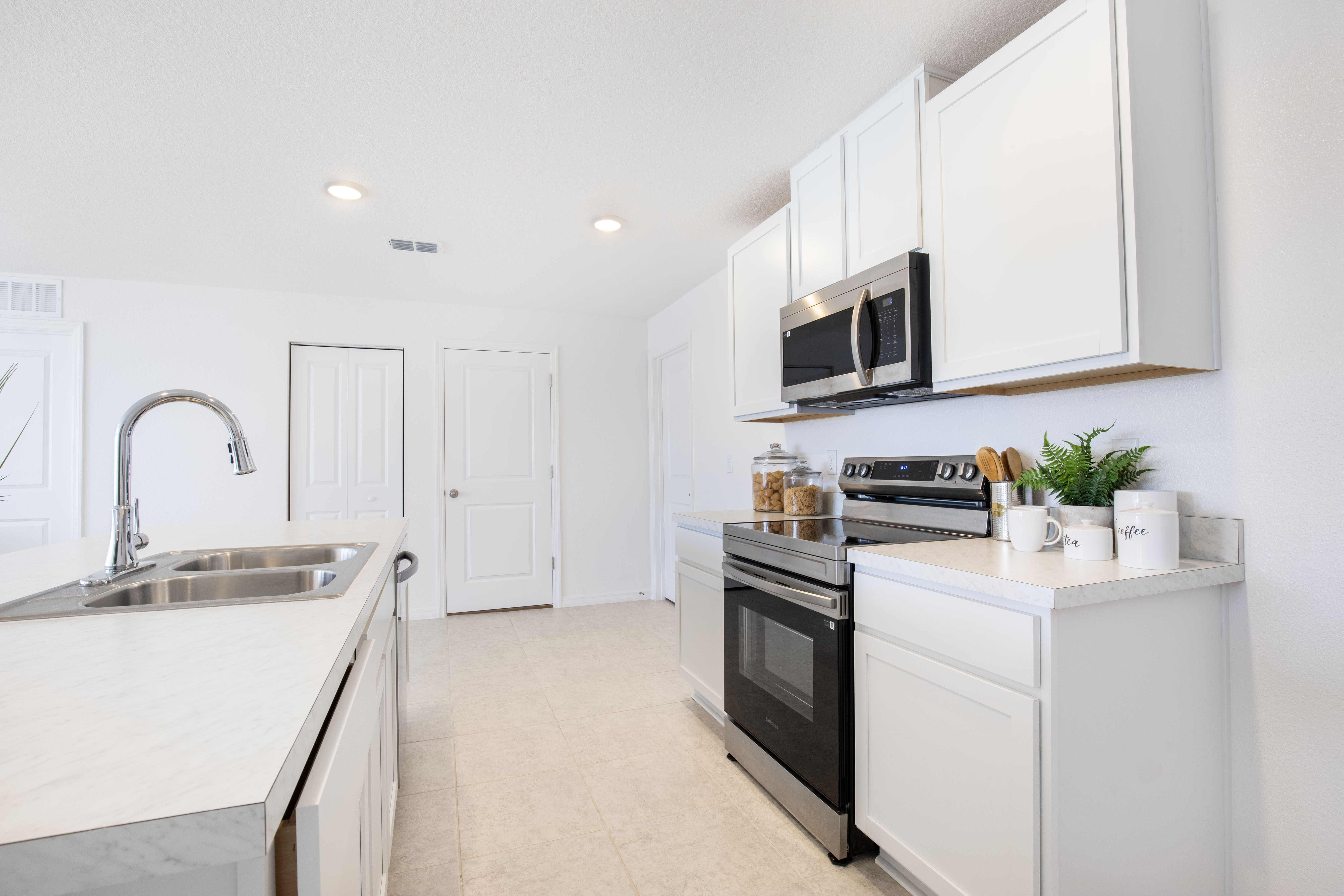 Modern white kitchen featuring stainless steel appliances, minimalist cabinets, and a sleek countertop with a double sink.