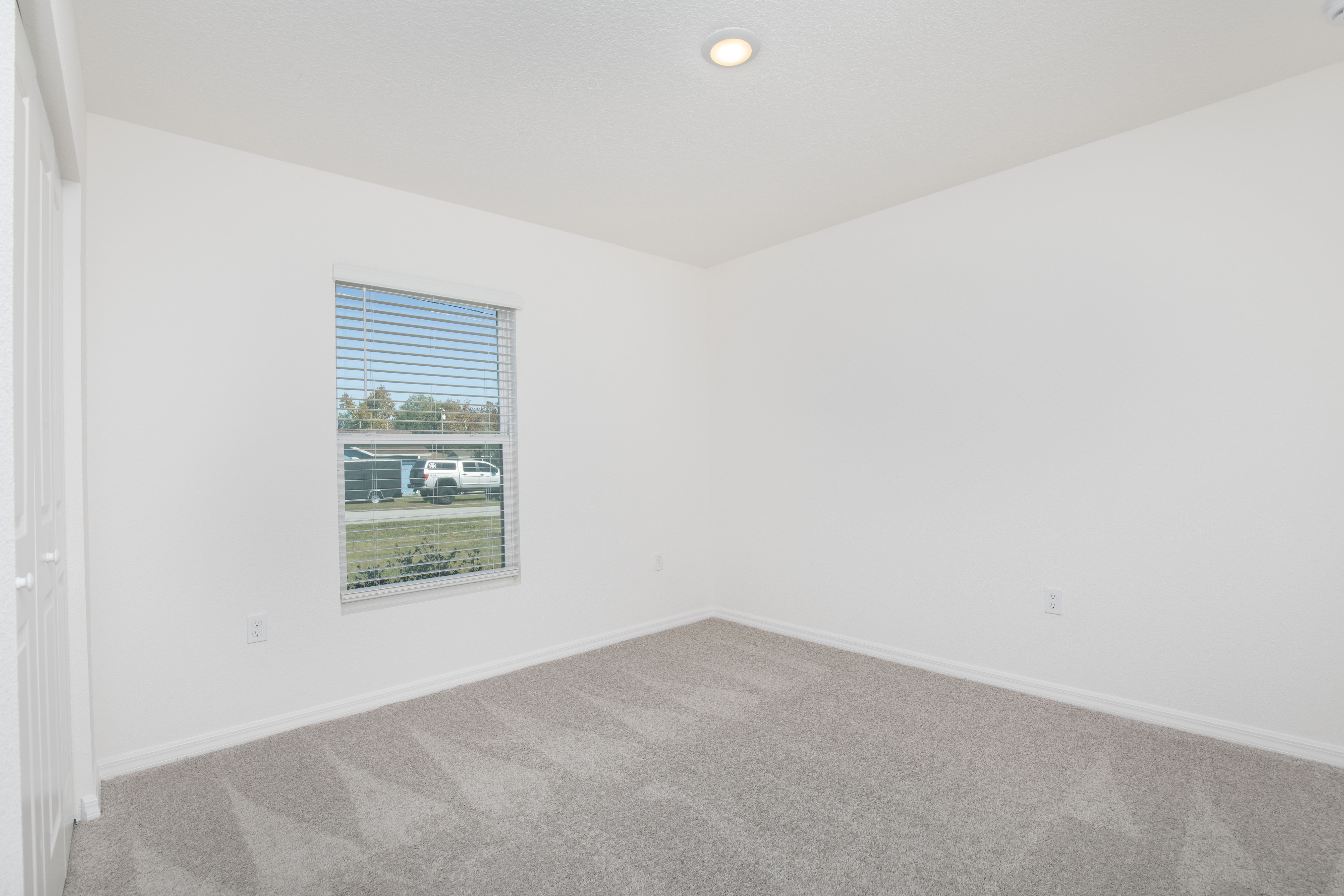 Empty white room with clean carpet and a single window with blinds on a sunny day.