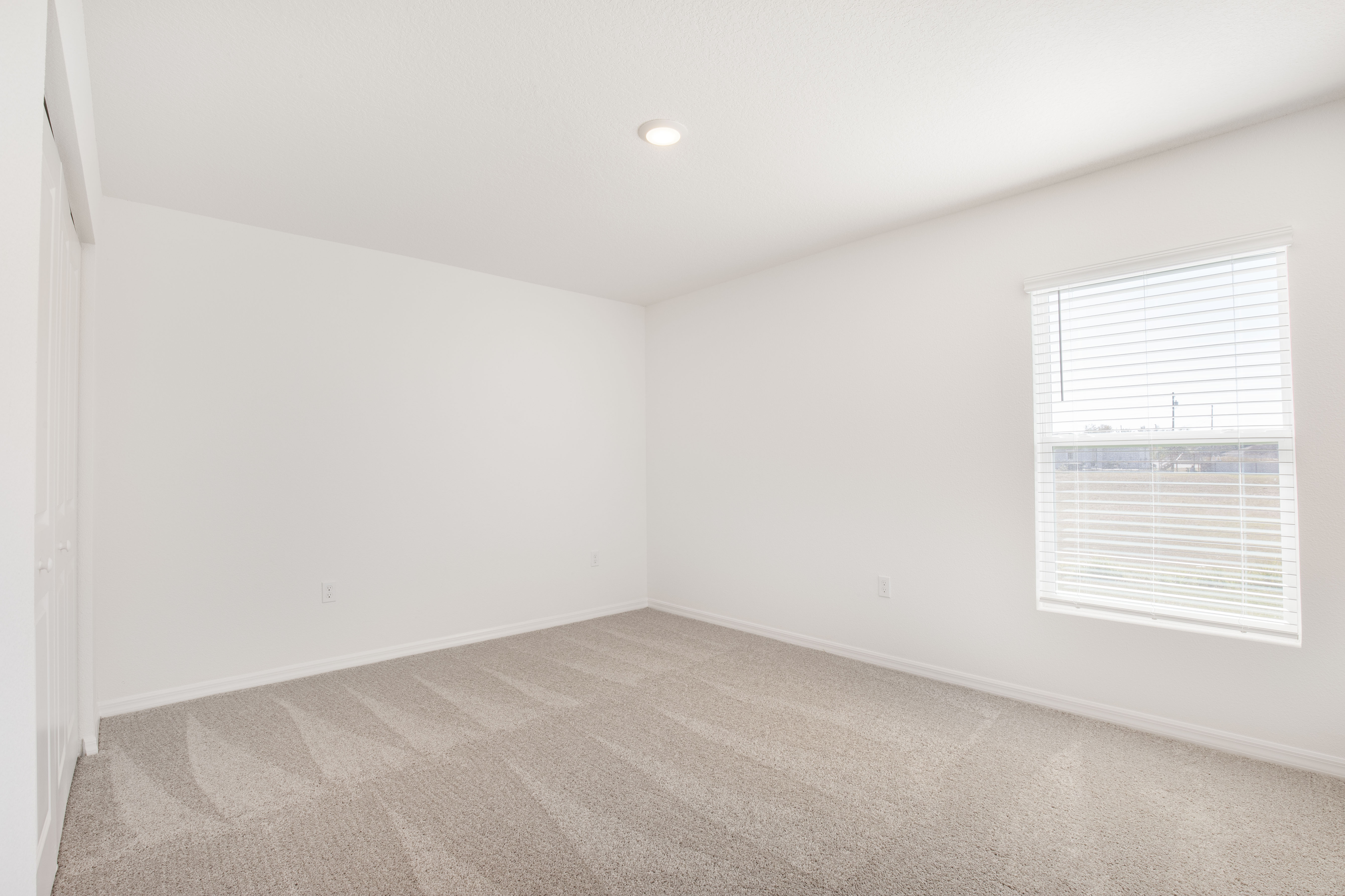 Alt tag: "Bright empty room with beige carpet, white walls, and a window with blinds."