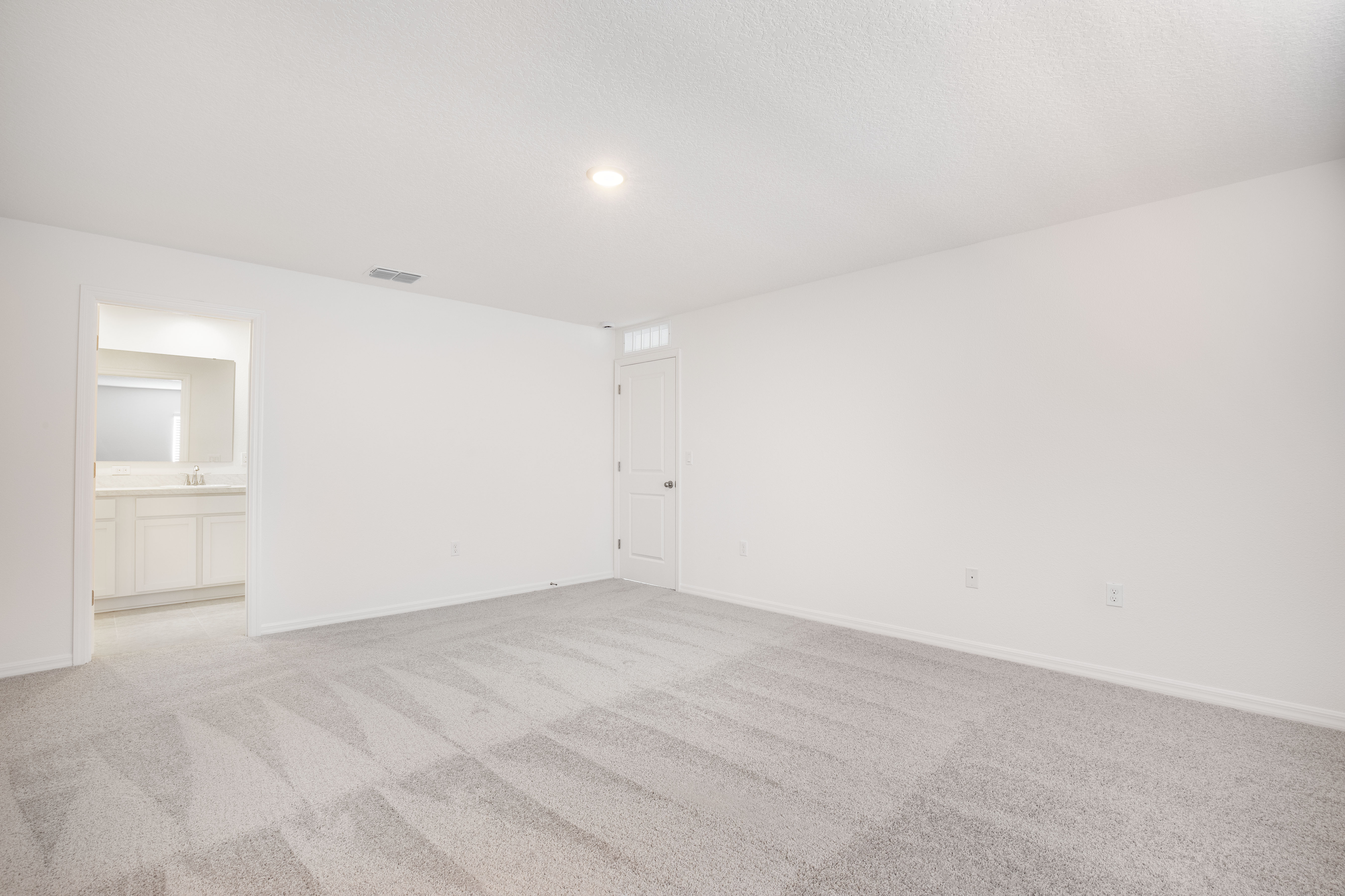 Empty room with clean carpet flooring, white walls, and a doorway leading to a bathroom.