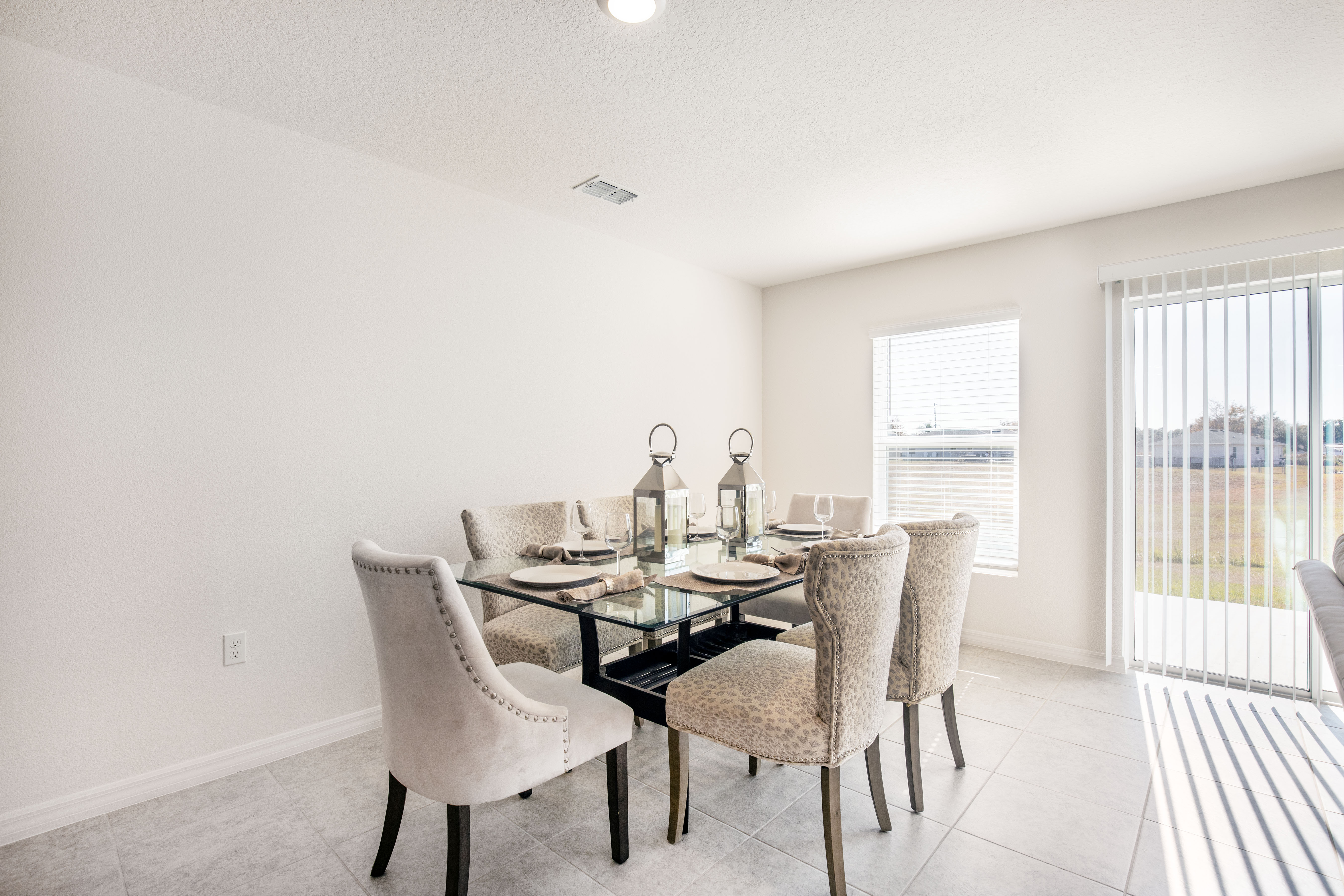 Modern dining room with a glass table, elegant upholstered chairs, and decorative lanterns by a bright window.