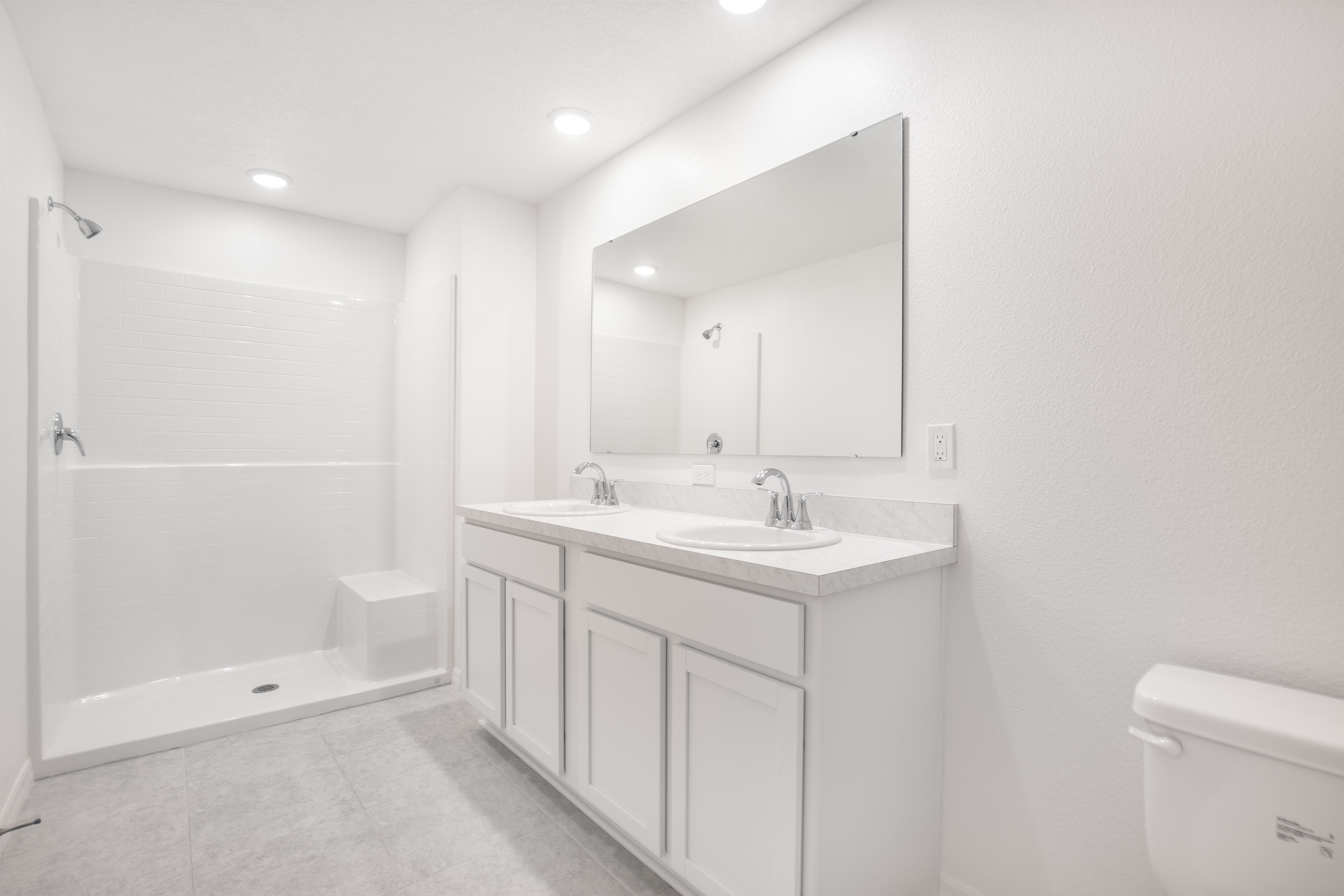 Modern white bathroom with double sinks, large mirror, and walk-in shower.