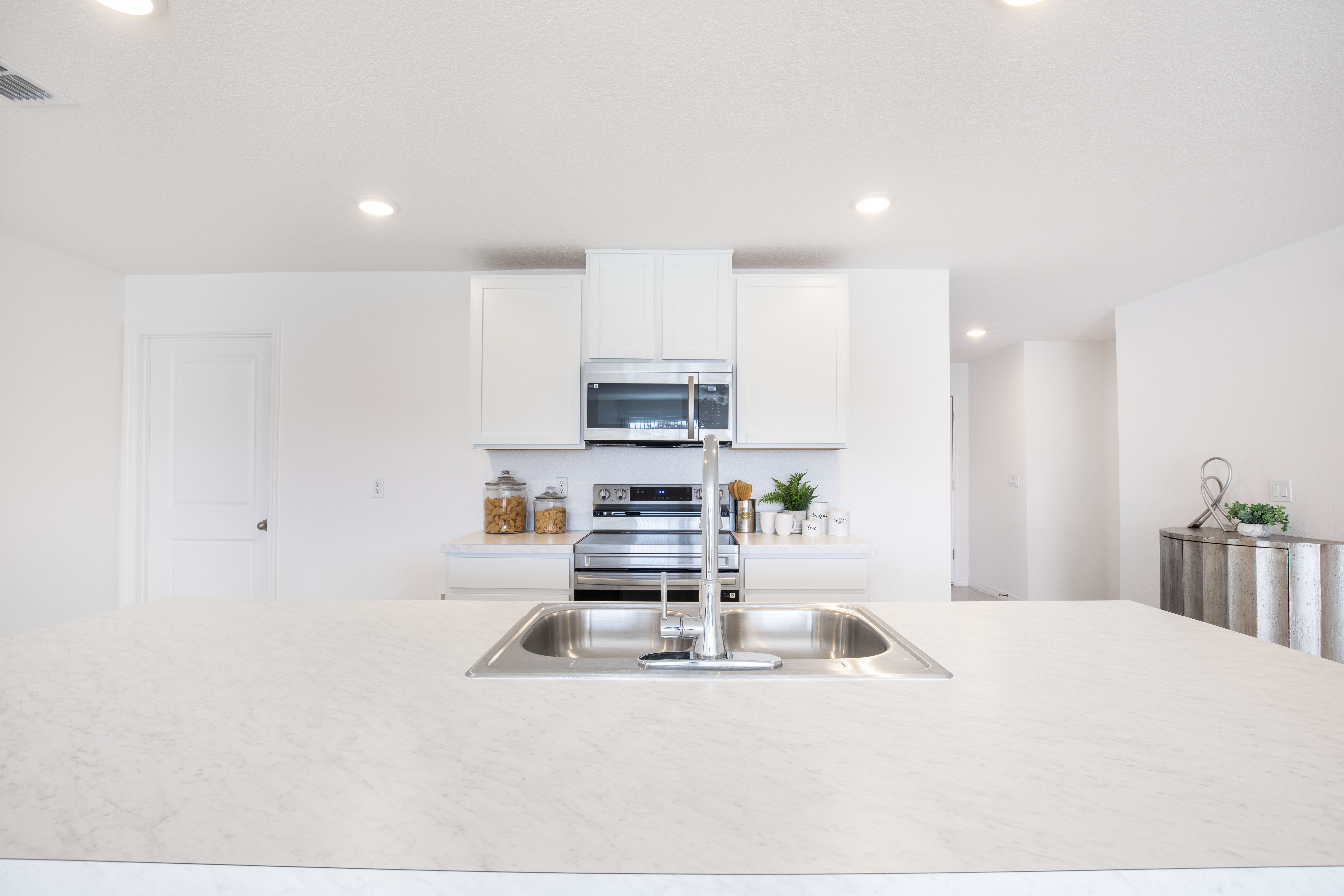 Modern kitchen with white cabinets, stainless steel appliances, and a marble countertop island featuring a double sink and faucet.