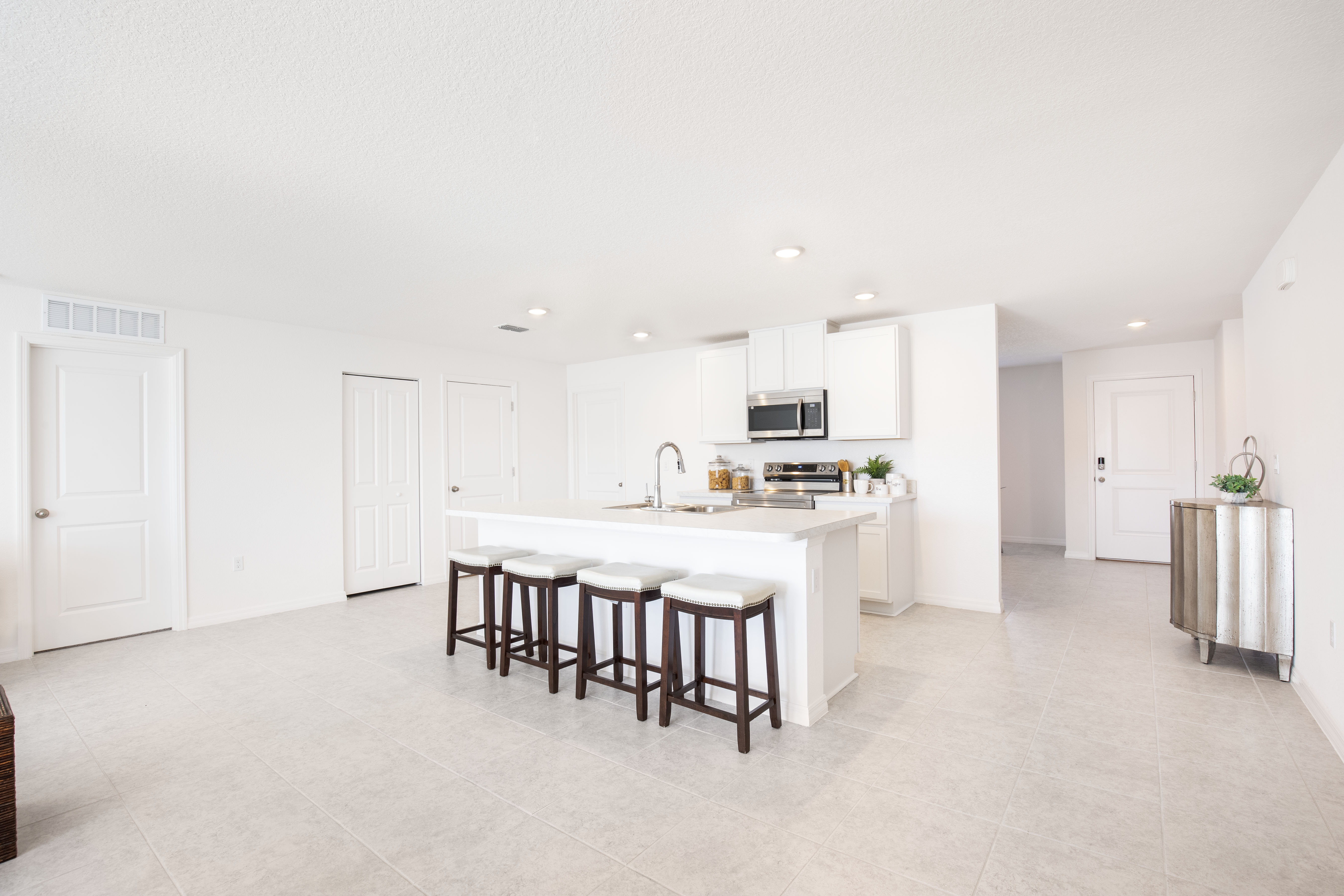 Modern kitchen interior with white cabinets, a central island with barstools, and stainless steel appliances.