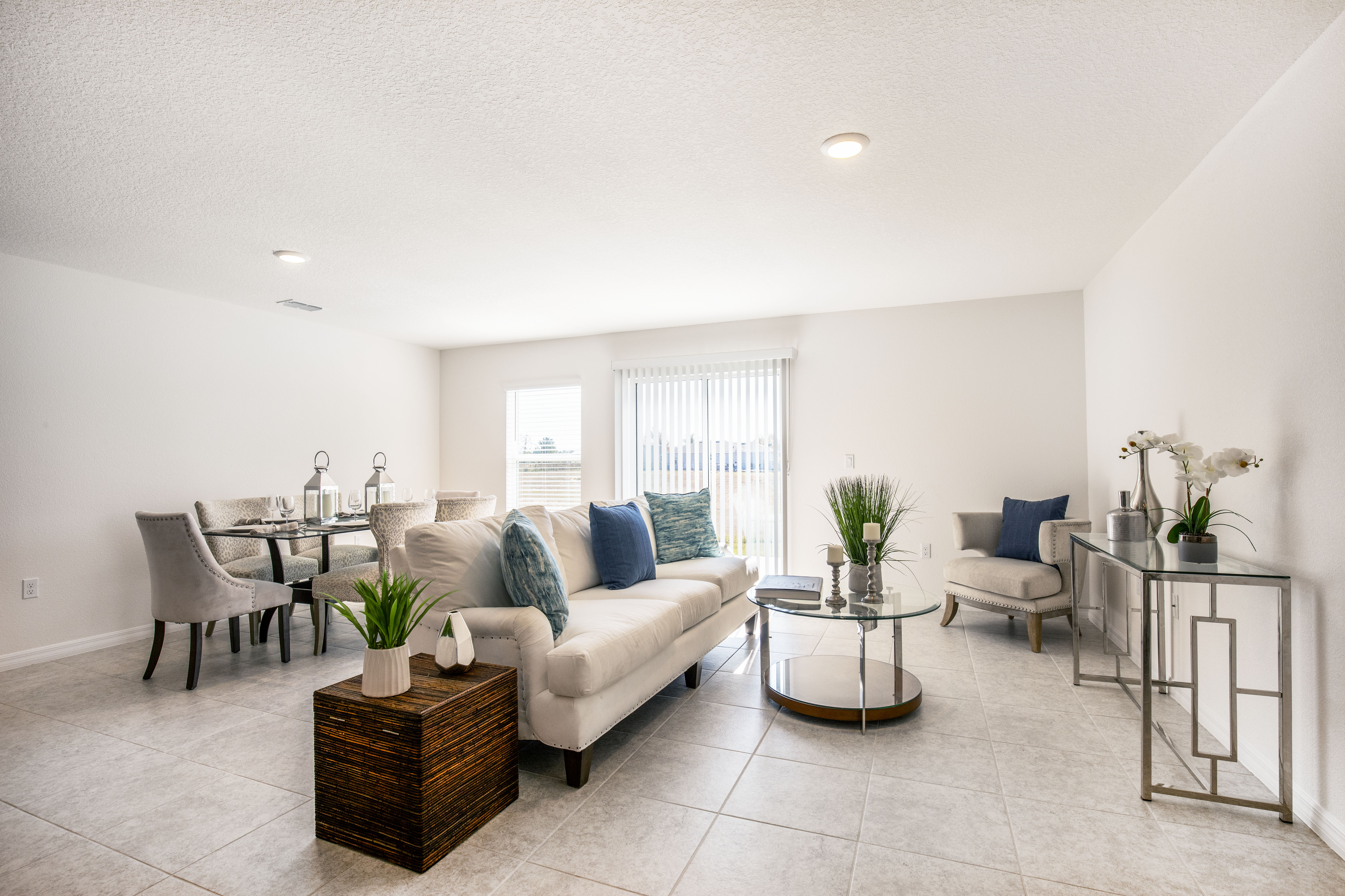 Modern living room with beige couches, glass coffee table, and elegant dining area, featuring minimalist decor and potted plants.