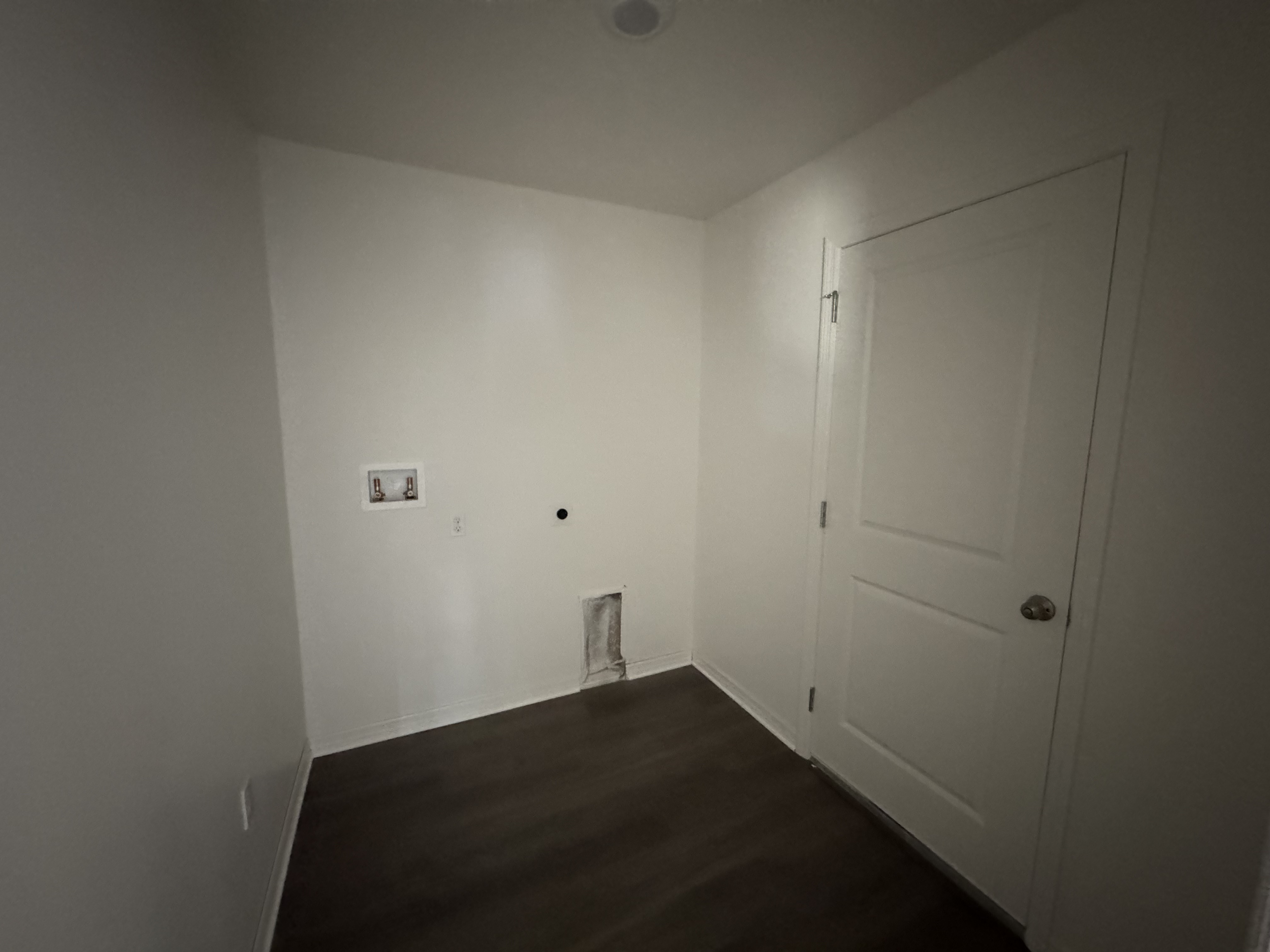 Empty laundry room with white walls, dark flooring, and plumbing hookups.