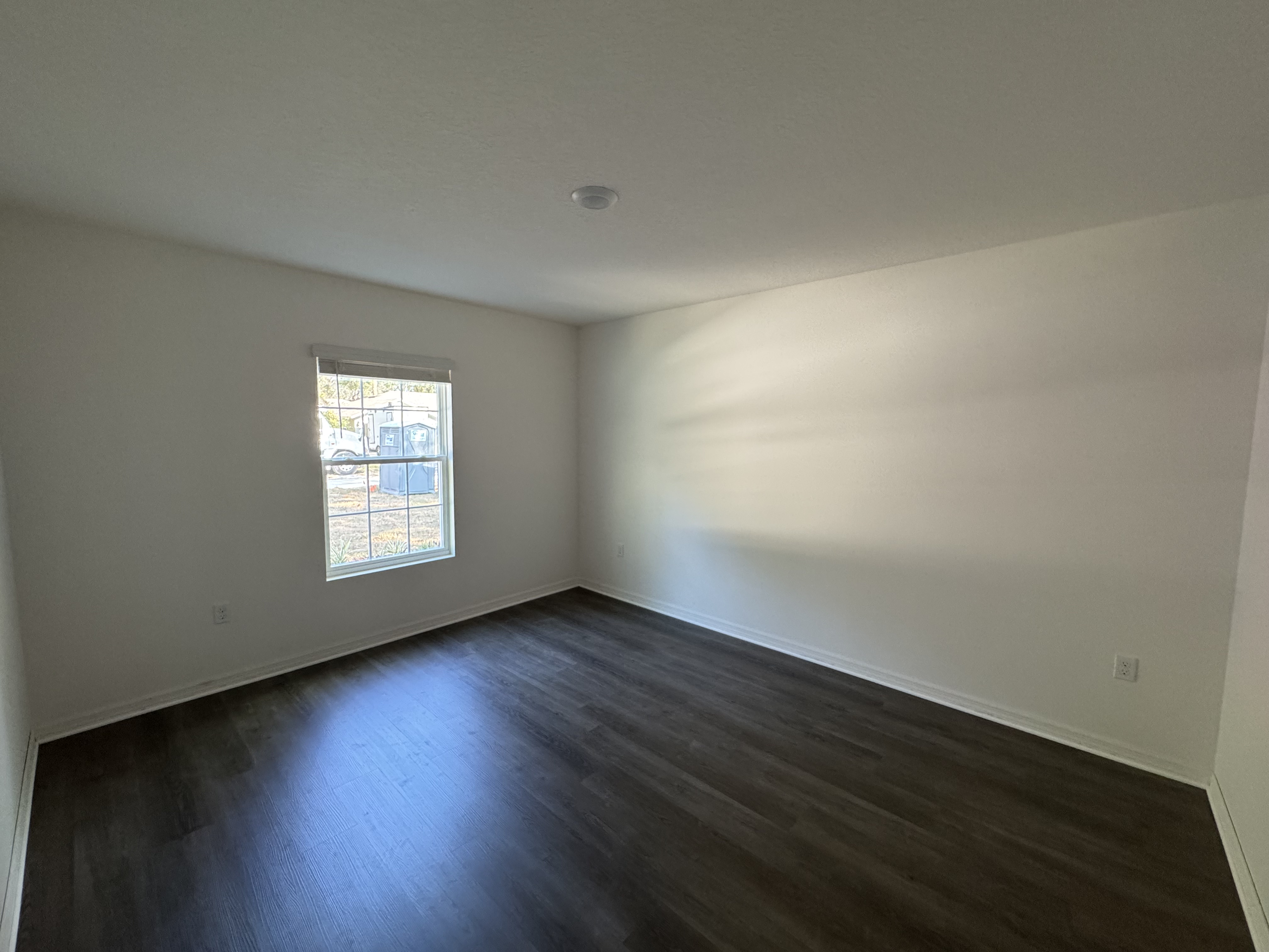 Empty room with dark hardwood flooring and a window letting in natural light.