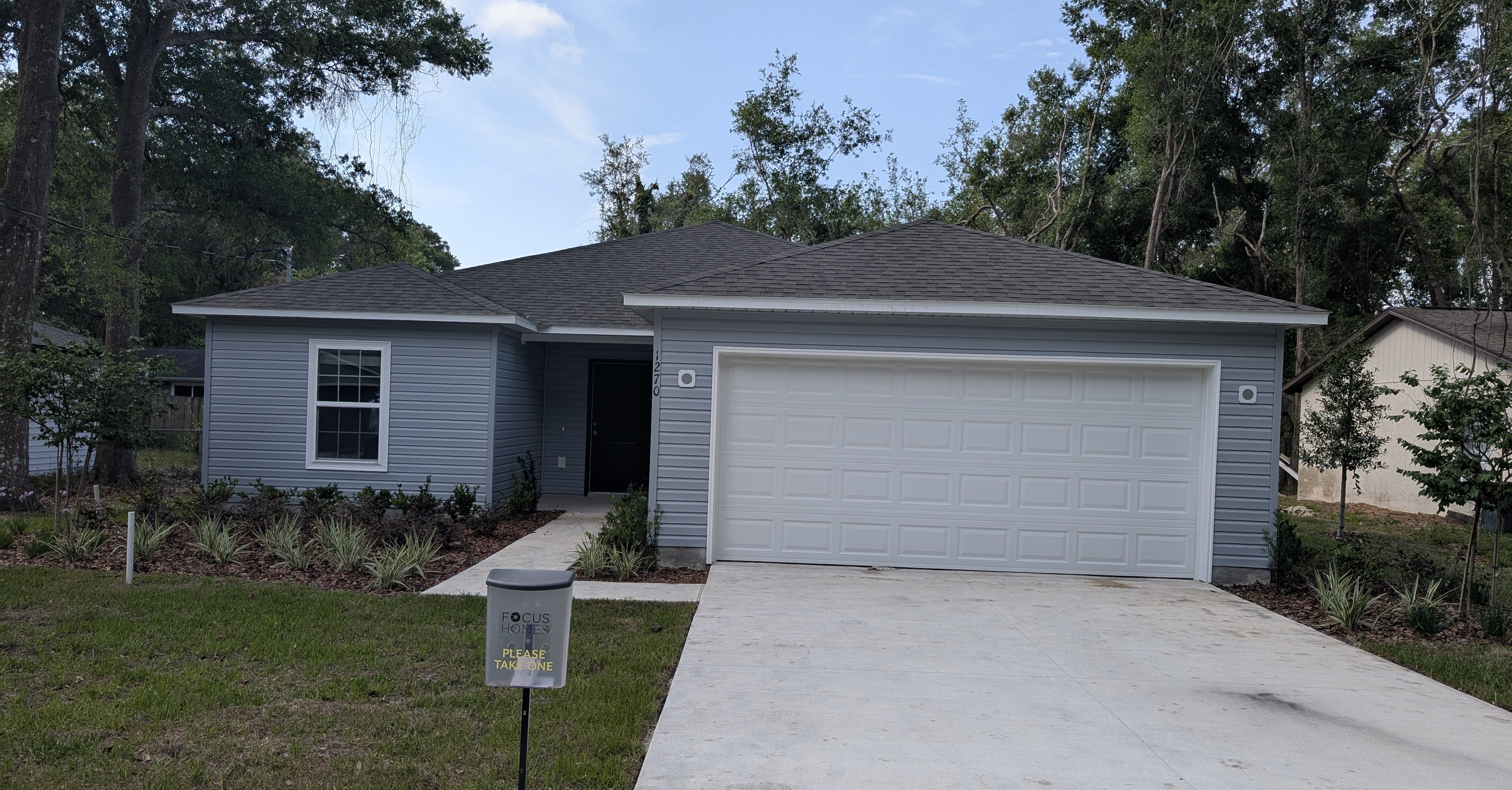 Single-story blue house with attached garage and landscaped front yard under a clear sky.