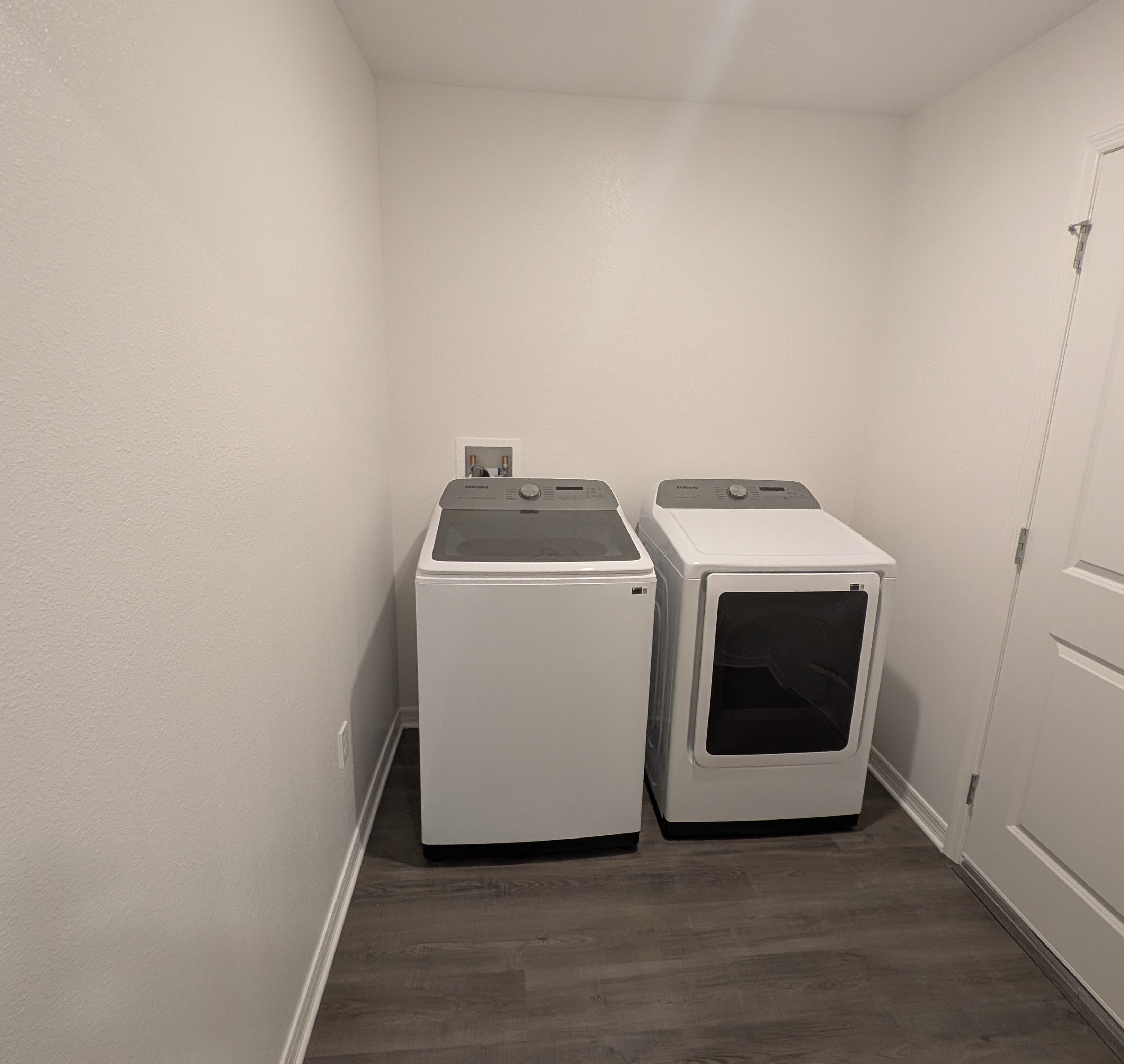 Modern laundry room with a white washer and dryer set on a dark wood floor.