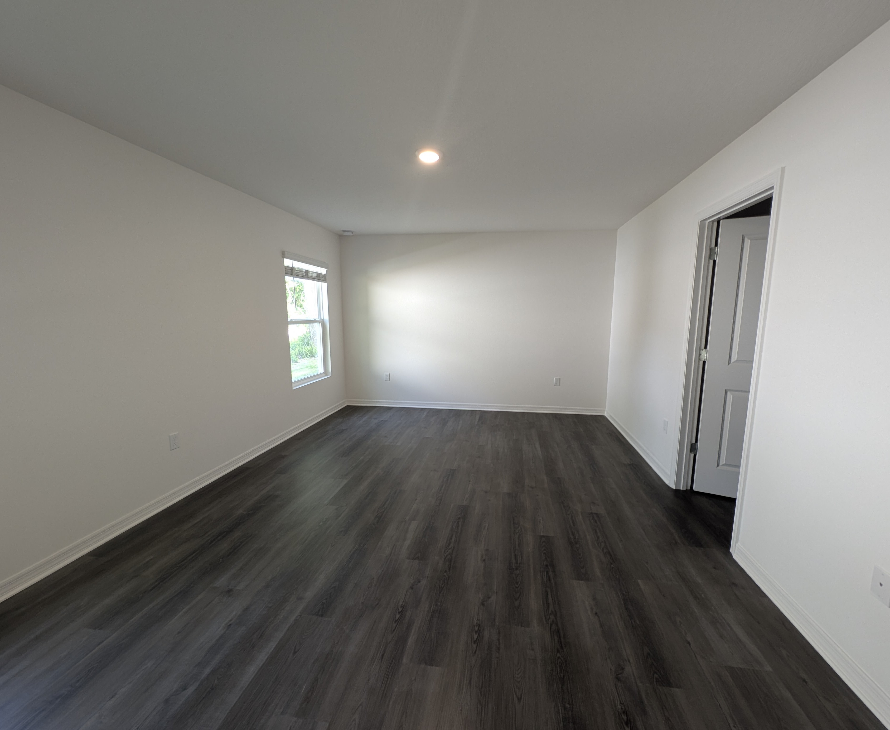 Modern empty room with dark wood flooring, white walls, and a single window letting in natural light.