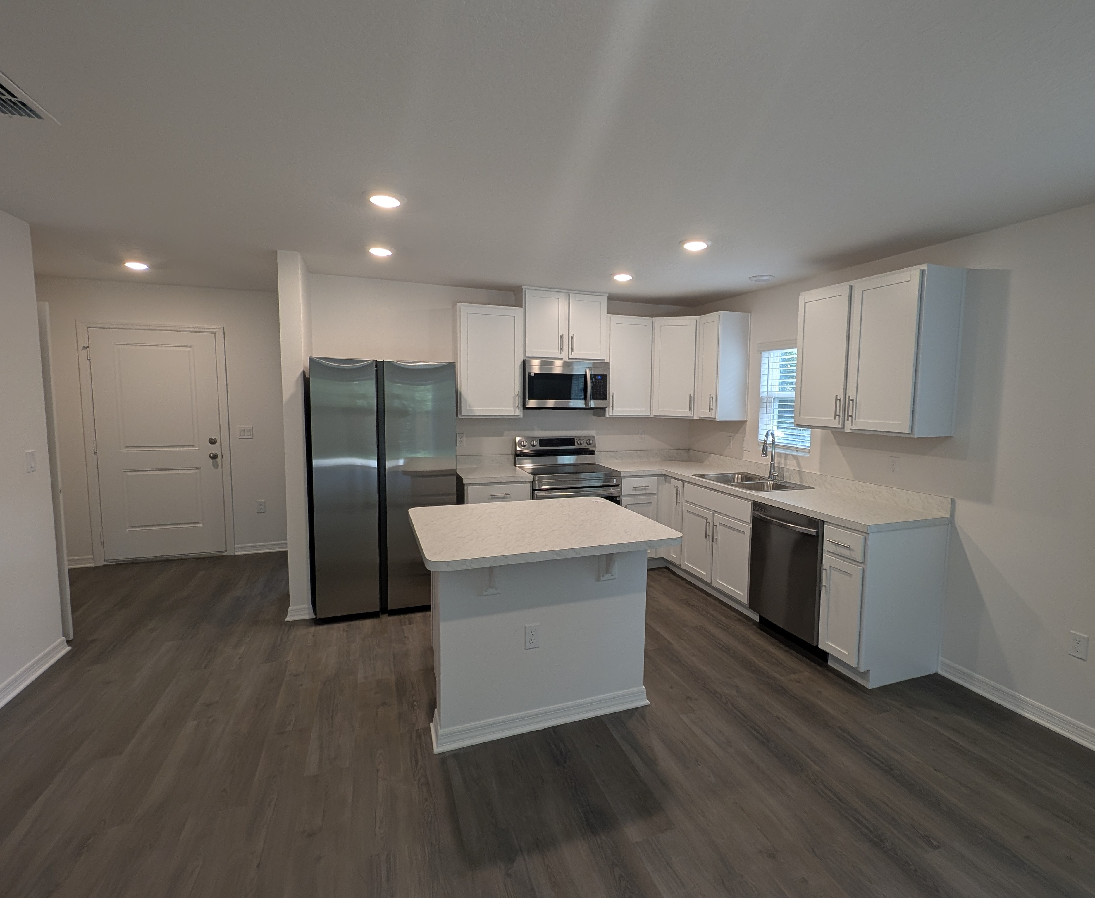 Modern kitchen with white cabinets, stainless steel appliances, and an island on wooden flooring.