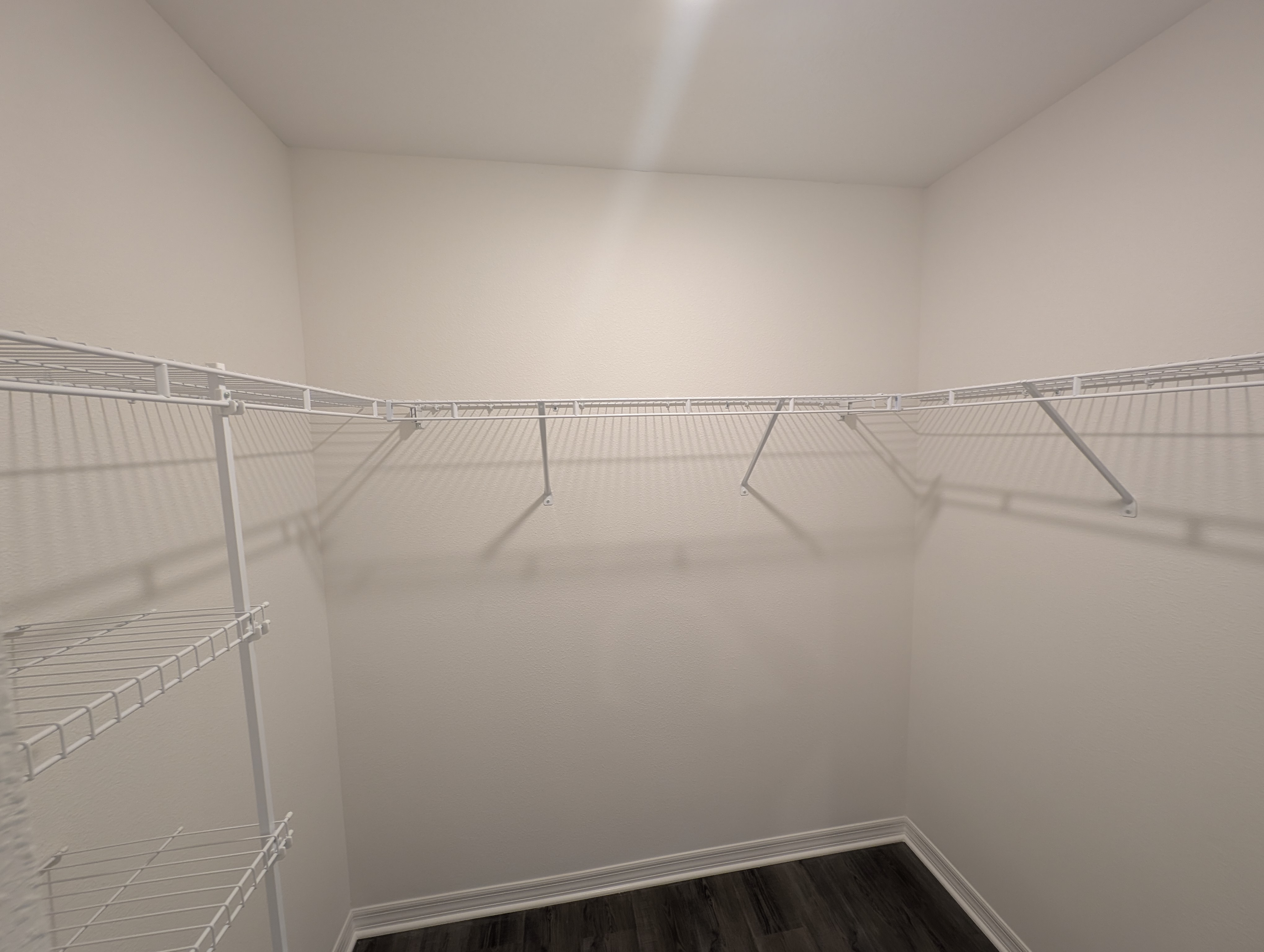 Spacious empty walk-in closet with white wire shelving and dark wood flooring.