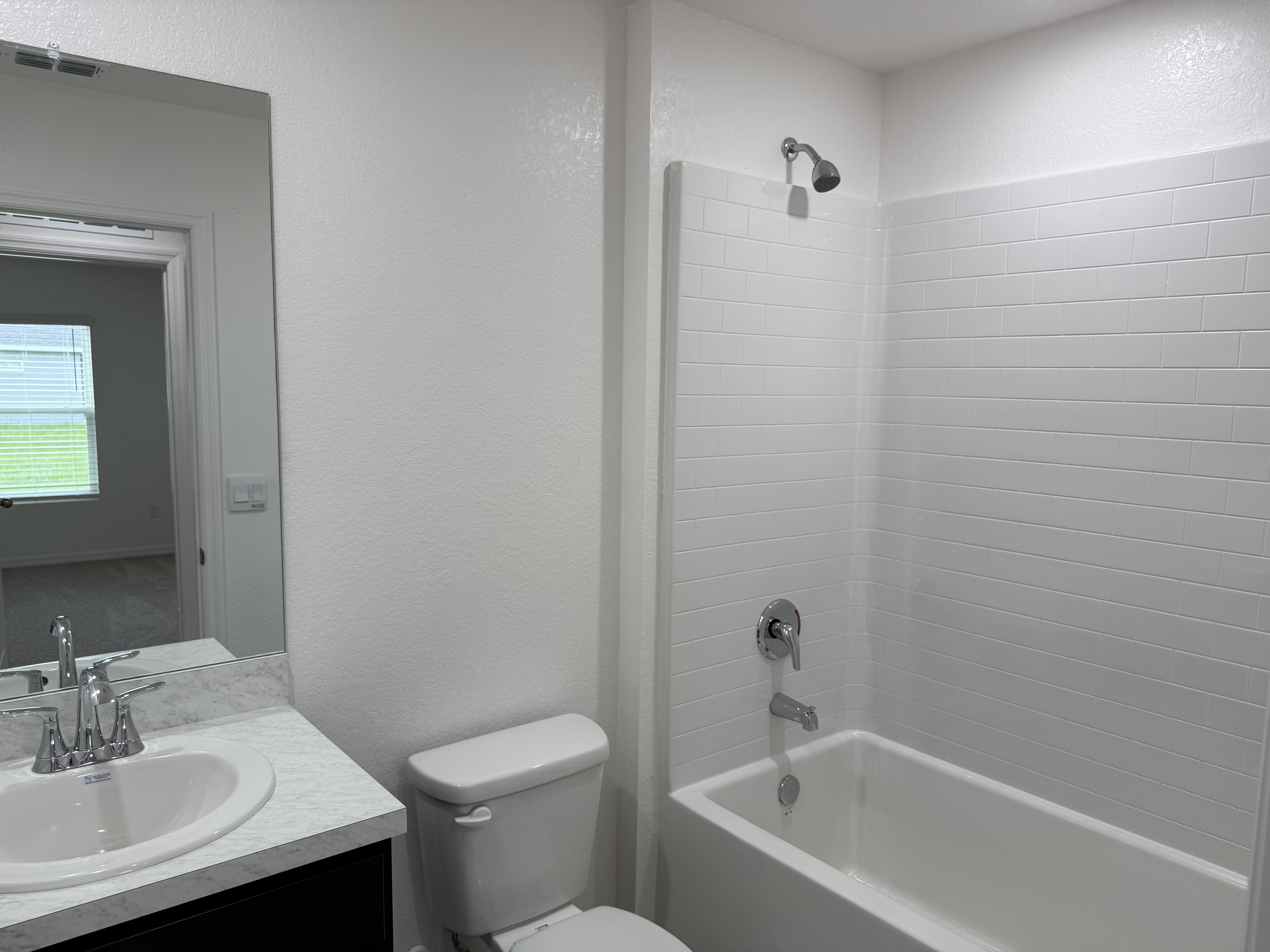Modern bathroom with a white bathtub and tiled shower, featuring a sink with a marble countertop, a mirror, and a toilet.