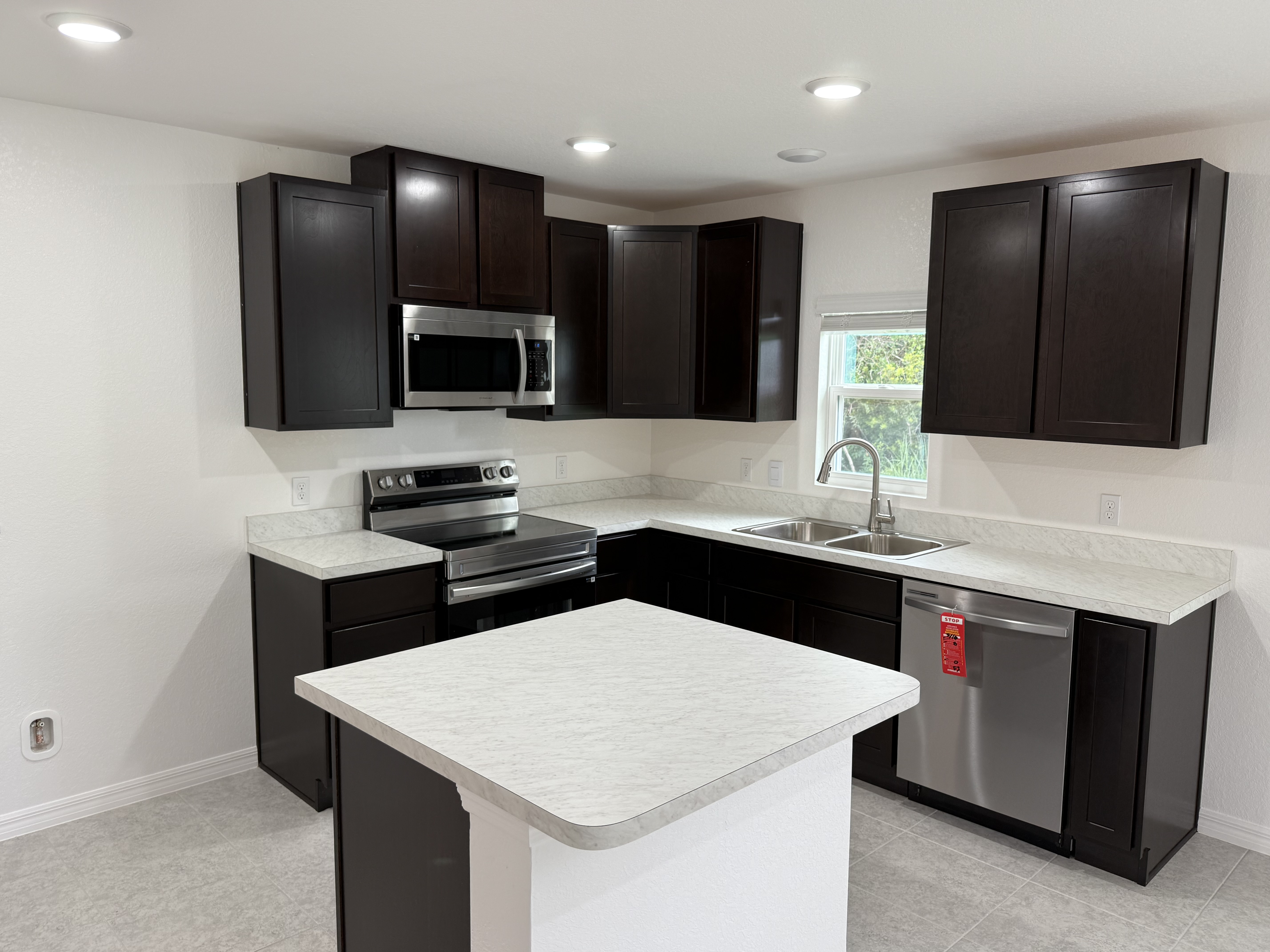 Modern kitchen with dark wood cabinets, stainless steel appliances, and a light marble countertop.
