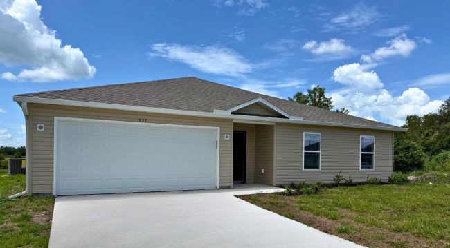 Modern single-story home with a two-car garage and well-maintained lawn under a clear blue sky.