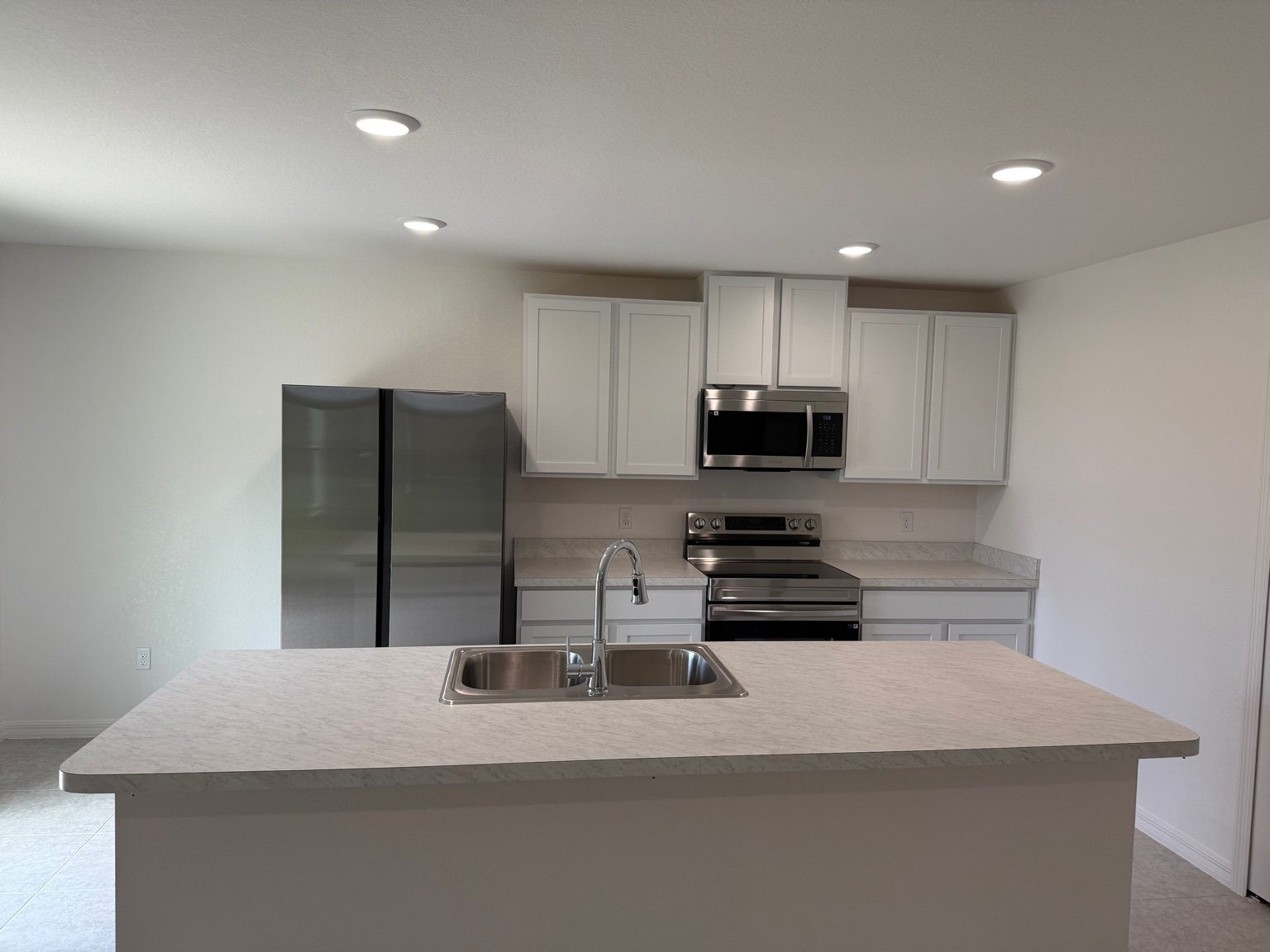 Modern kitchen with white cabinets, stainless steel appliances, and a large island countertop featuring a sink.