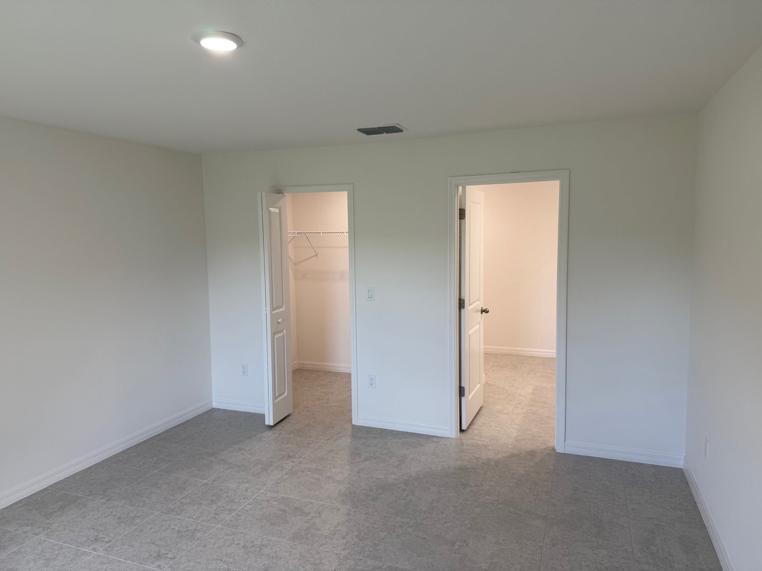 Empty room with gray tiled flooring, white walls, and two doorways leading to a closet and another area.