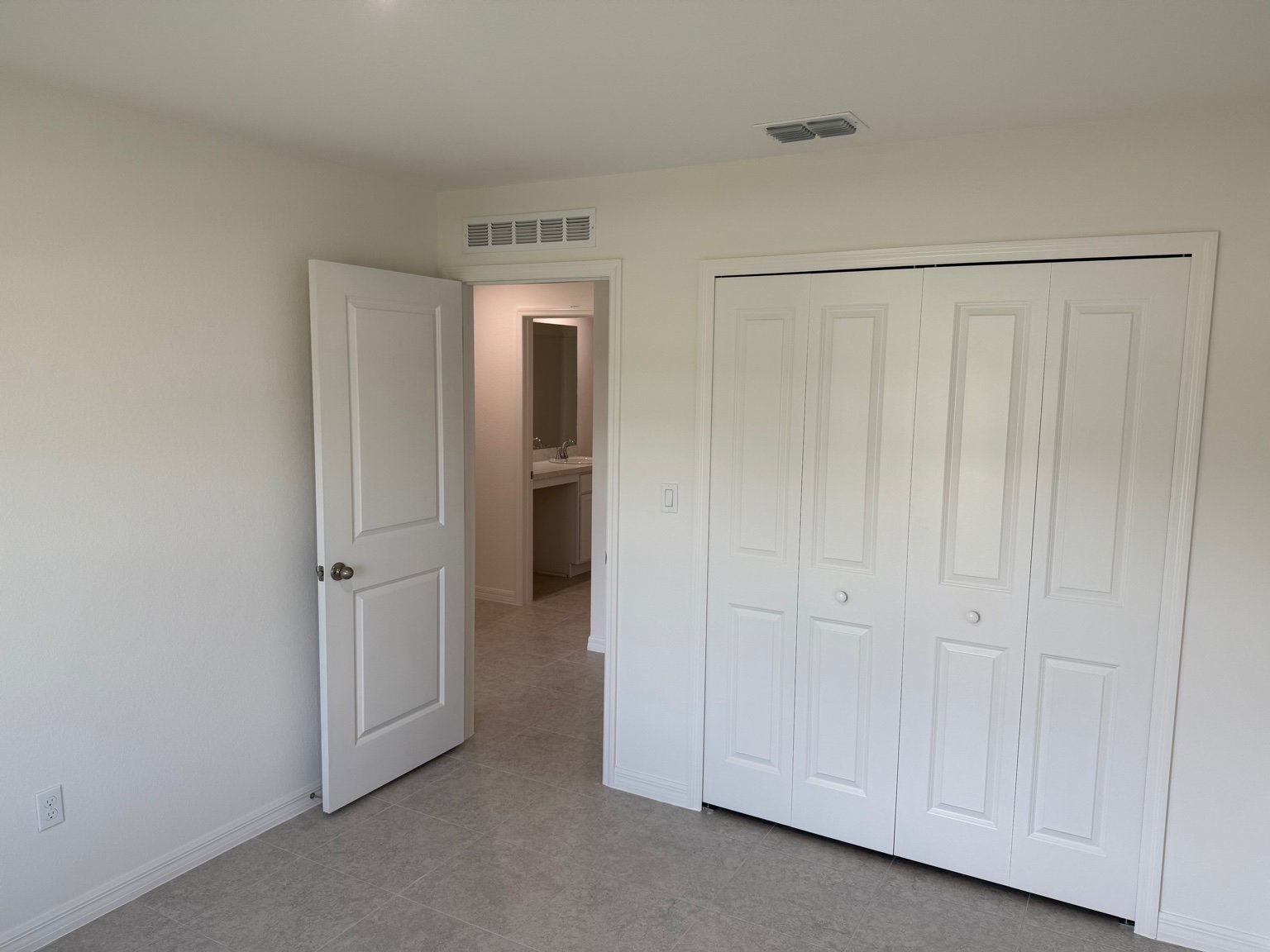 Empty room with white walls, an open door leading to a bathroom, and a closed closet door.