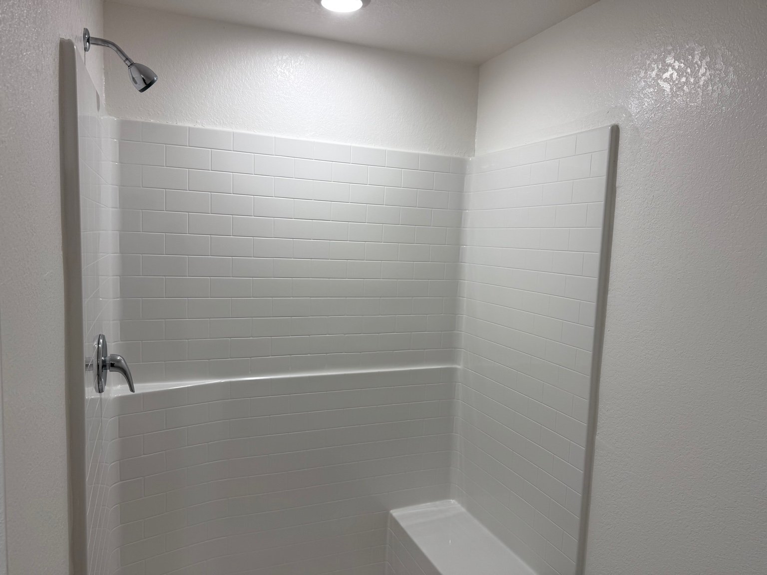 Modern white tiled shower with a bench and chrome fixtures in a brightly lit bathroom.