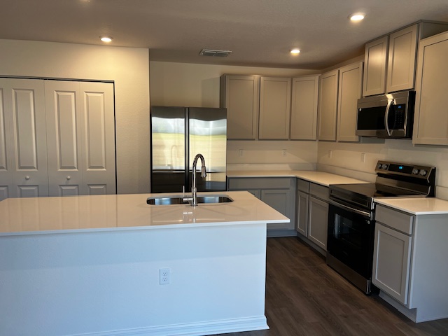 Modern kitchen with gray cabinets, stainless steel appliances, and a central island with a sink.
