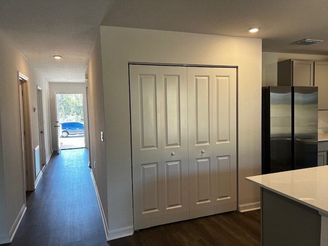 Modern kitchen entrance with white cabinets and stainless steel fridge in a newly renovated home.