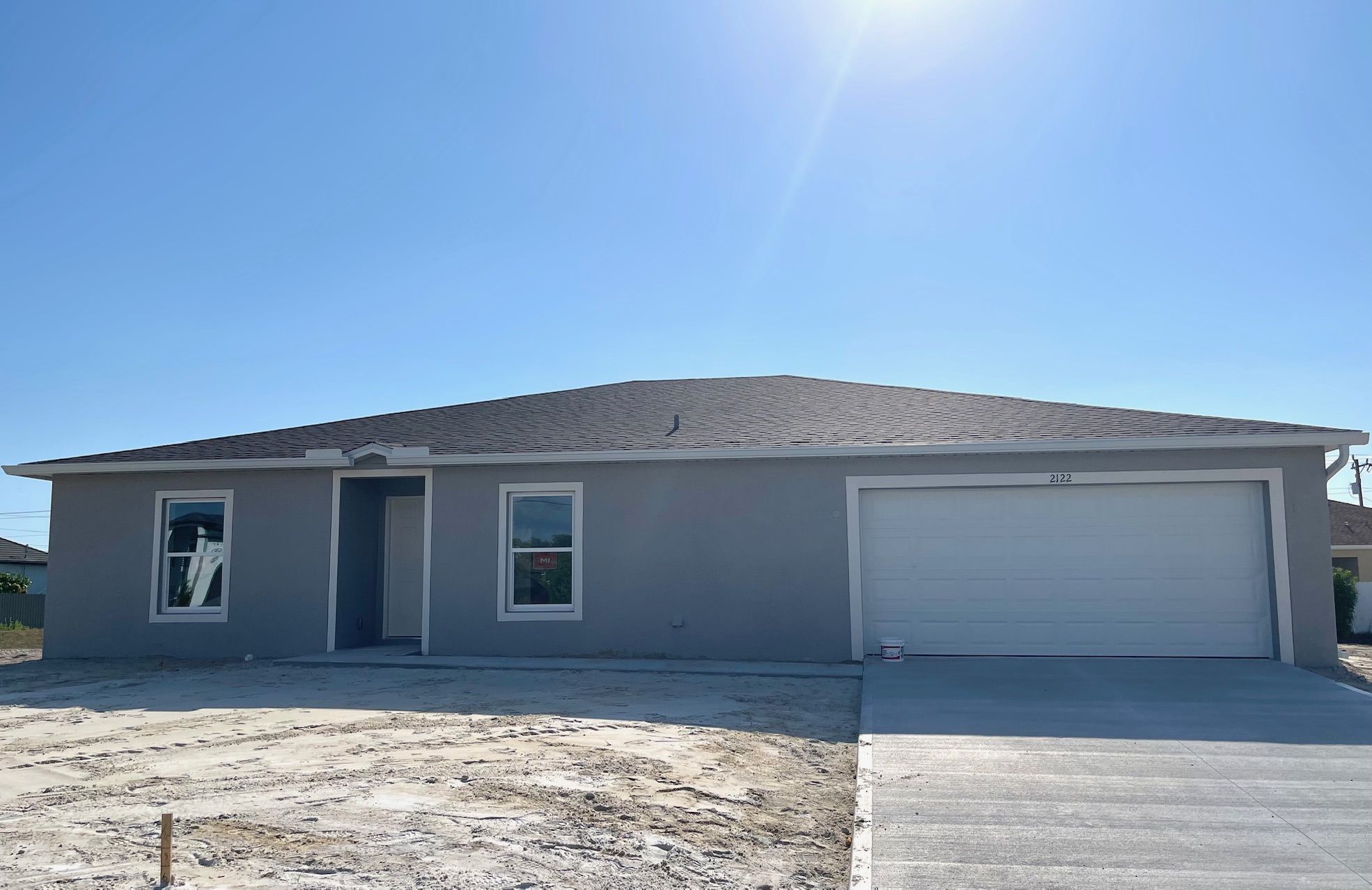 Newly constructed single-story grey house with a two-car garage under a clear blue sky.