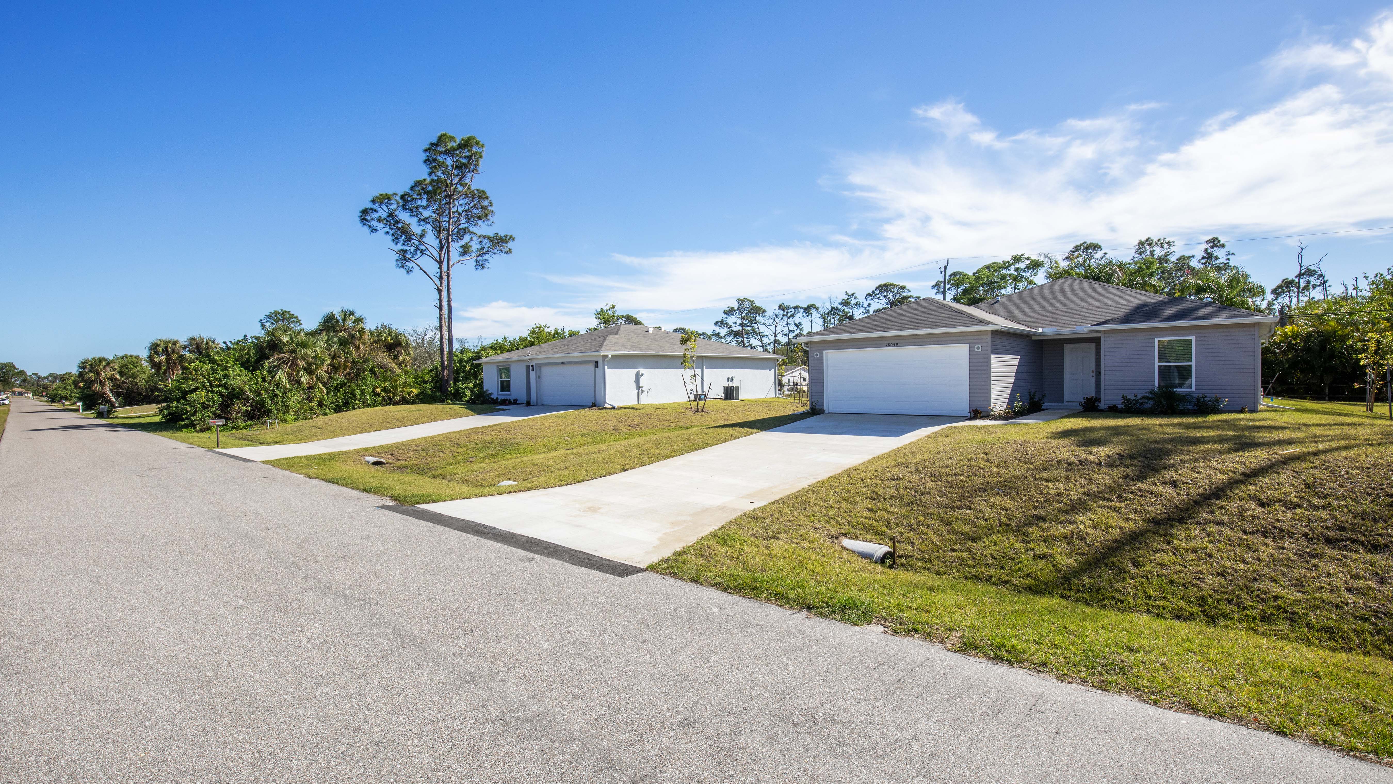 Suburban street view featuring two single-story homes with driveways and manicured lawns under a clear blue sky.