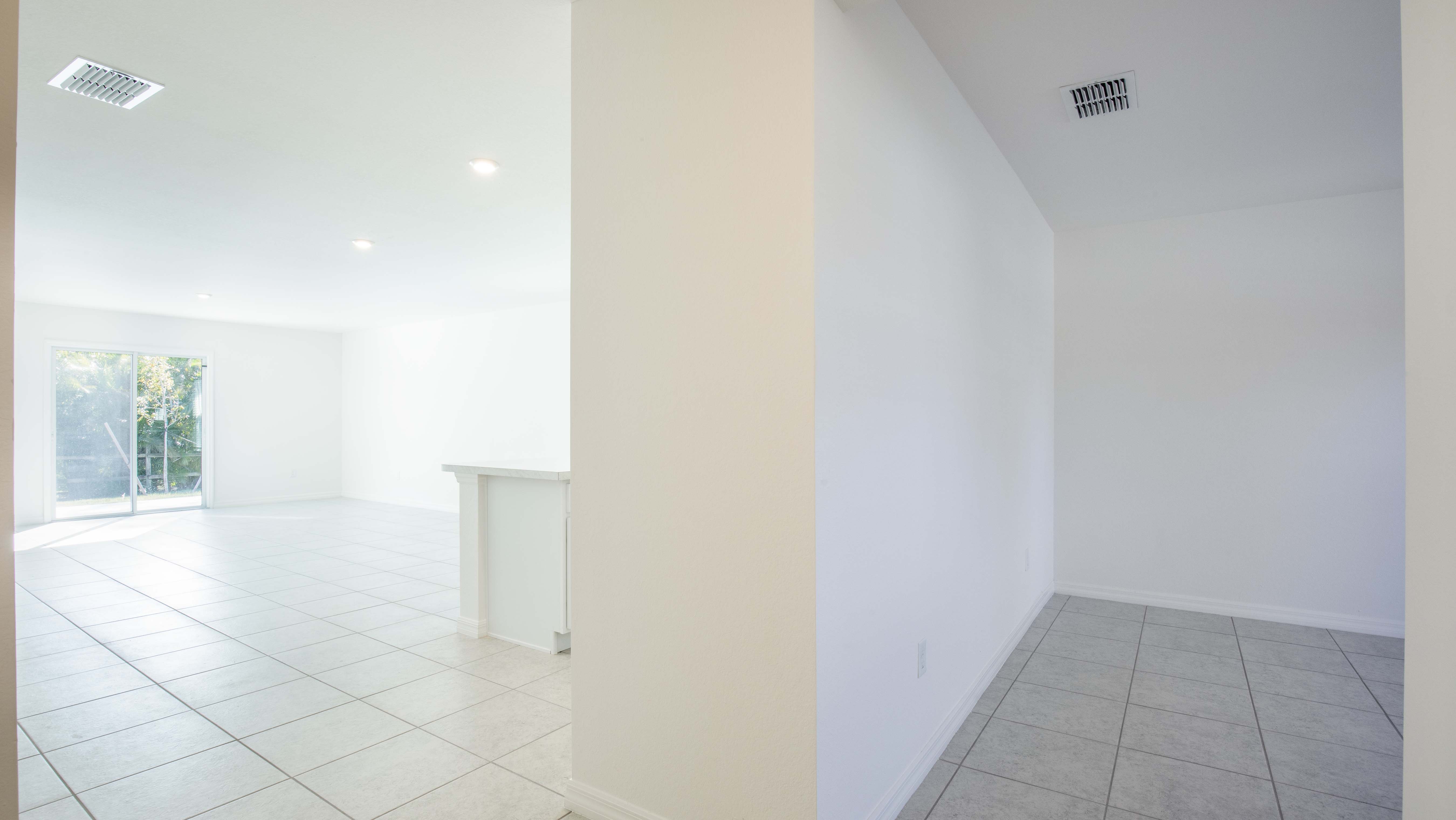 Bright, spacious empty room with tiled floors and large sliding glass doors allowing natural light.