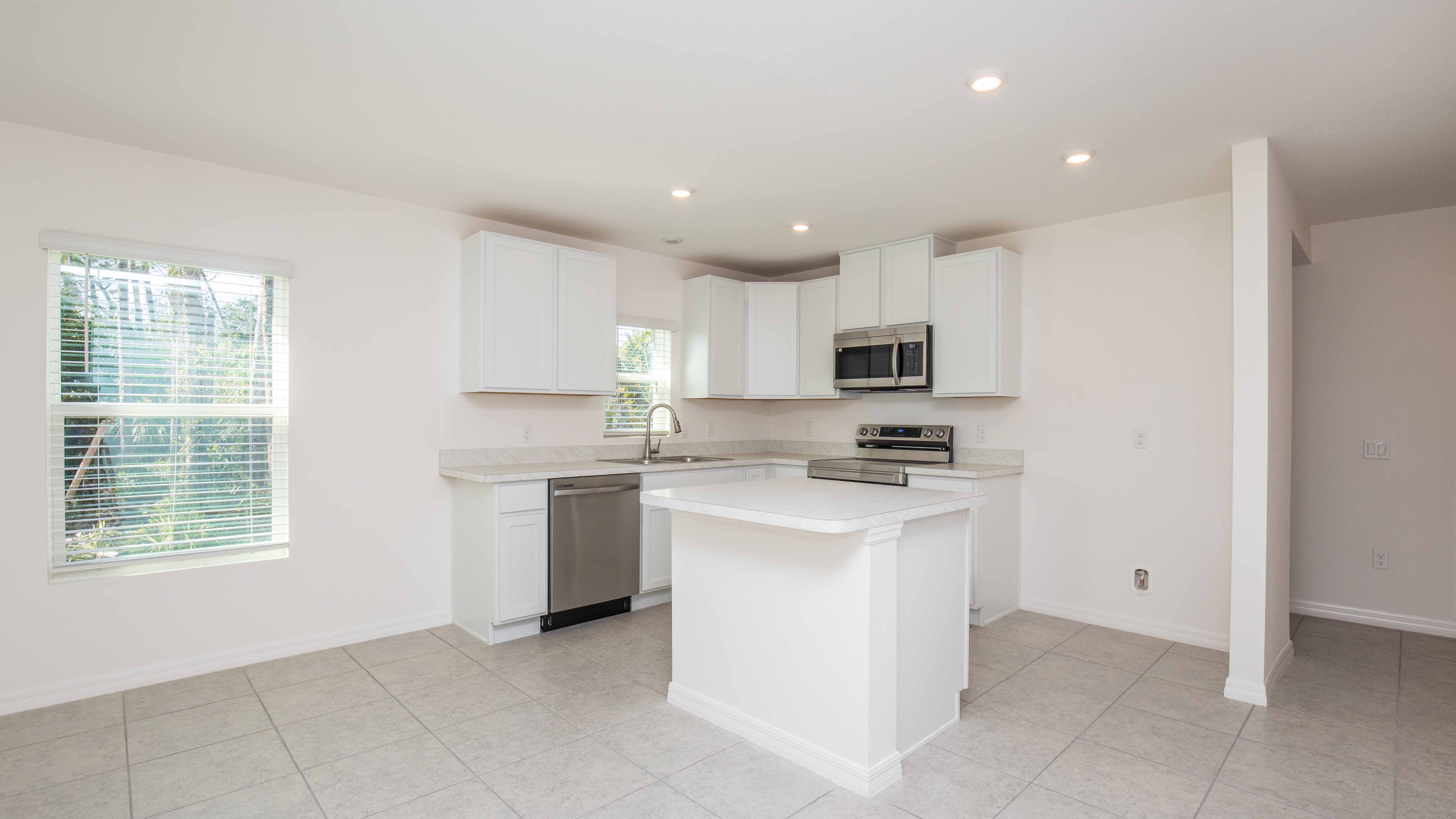 Modern kitchen with white cabinets, stainless steel appliances, and a central island in a bright, open space with tile flooring.