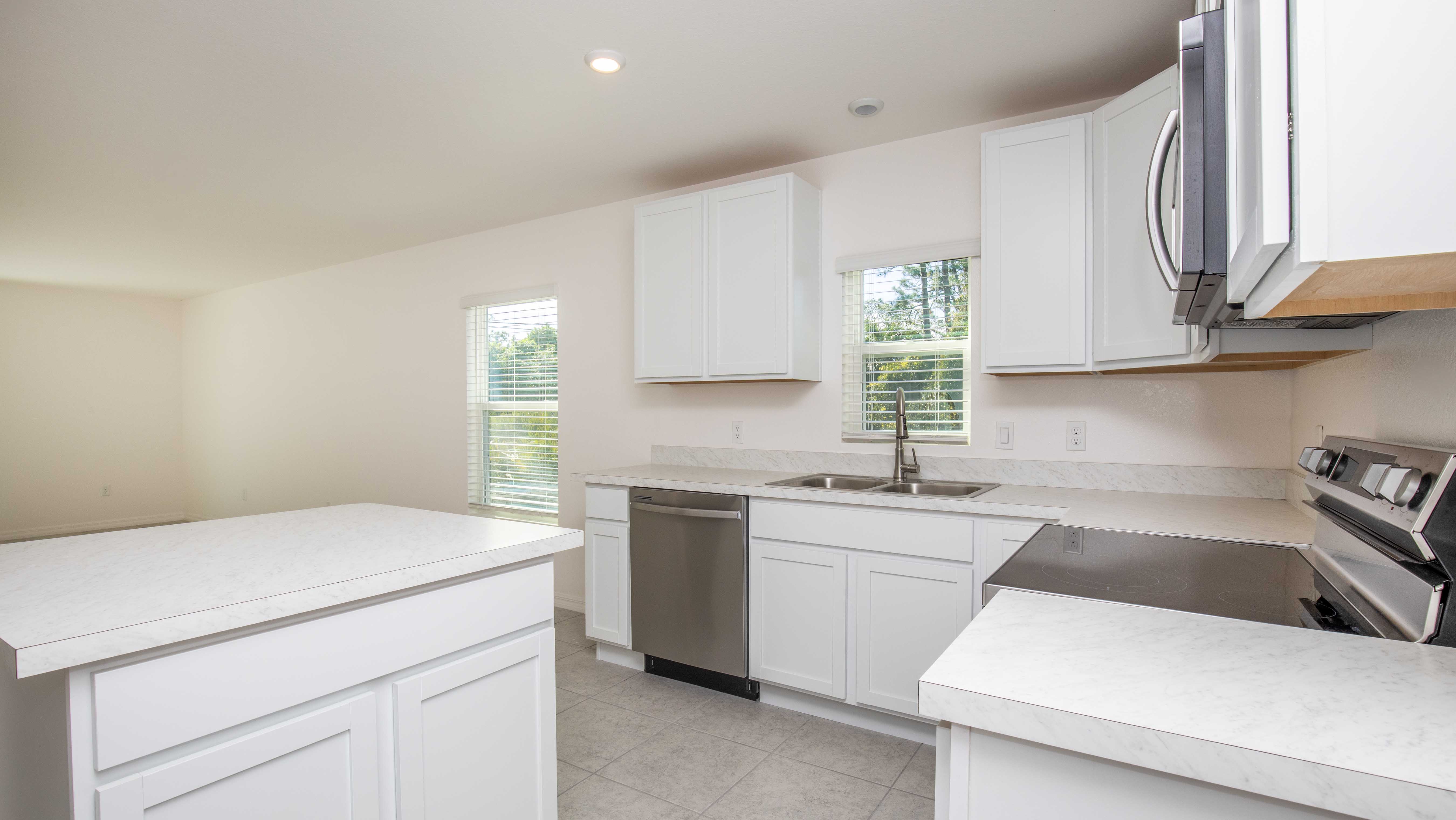 Modern kitchen interior with white cabinets, stainless steel appliances, and natural light through large windows.