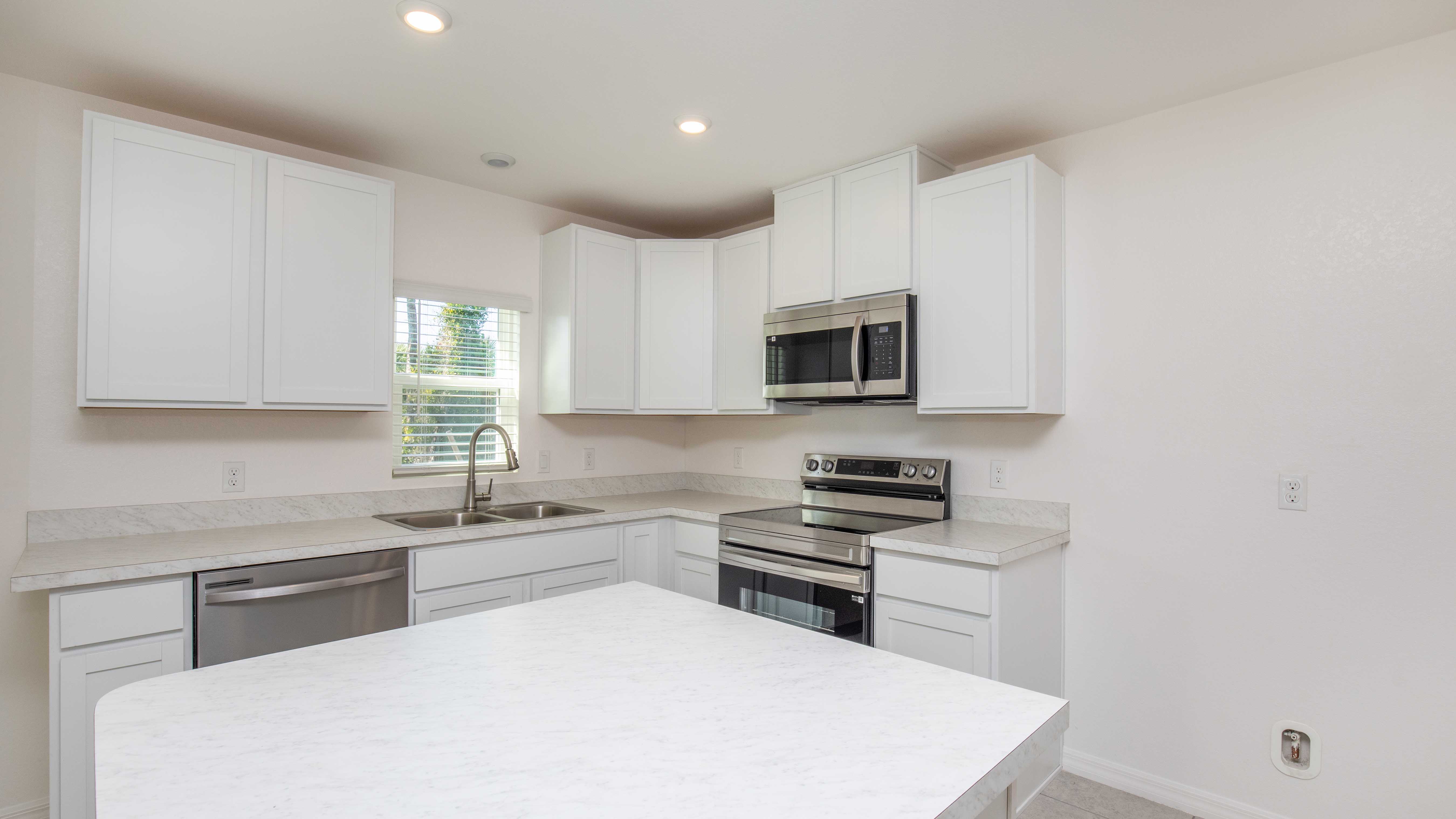 Modern kitchen with white cabinetry, marble countertops, stainless steel appliances, and a centered island.