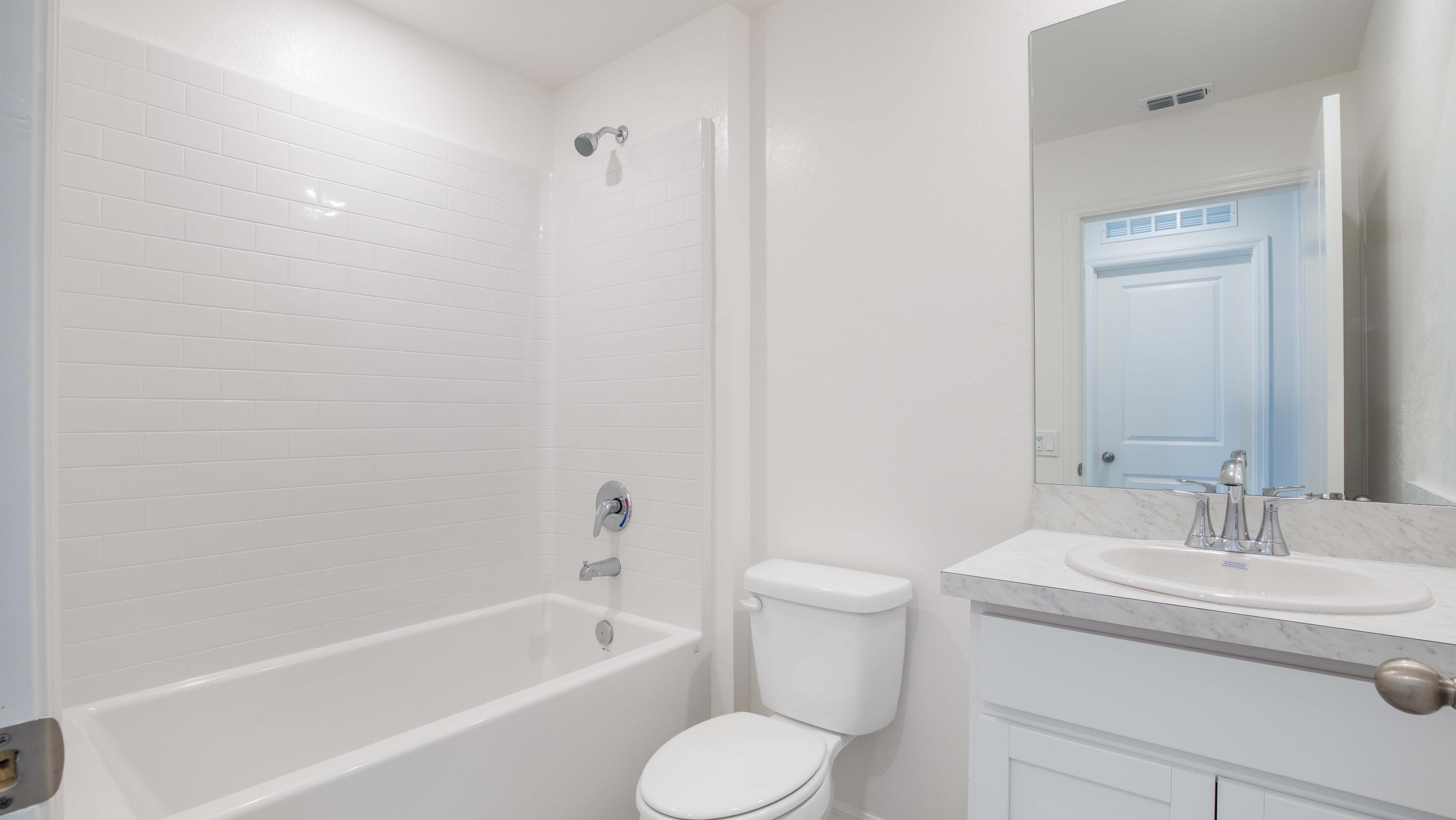Modern, bright white bathroom with sleek bathtub, toilet, and marble sink countertop.