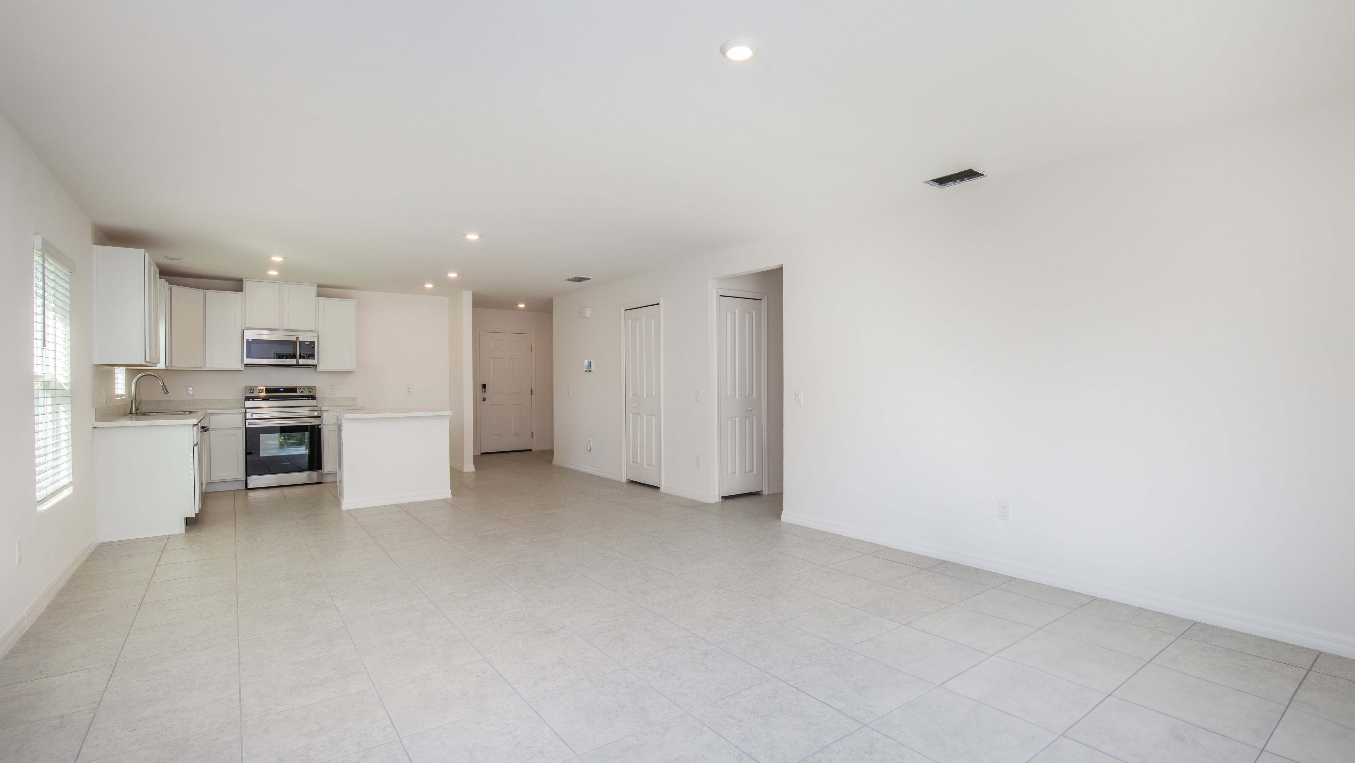 Modern open-concept kitchen and living area with light tile flooring, white cabinets, and stainless steel appliances.