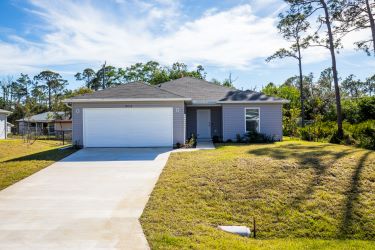 Modern single-story home with a two-car garage and well-maintained lawn under a clear blue sky.