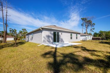 A single-story home with a gray exterior featuring large backyard under a clear blue sky.