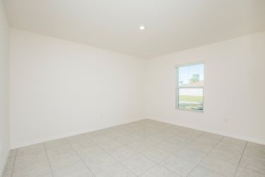 Bright, empty room with tiled flooring and a large window allowing natural light.