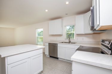 Modern white kitchen with stainless steel appliances, large windows, and ample counter space.