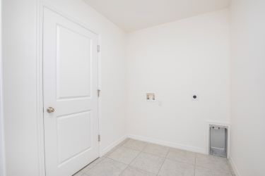 Minimalist white laundry room with tiled floor and space for washer and dryer installation.