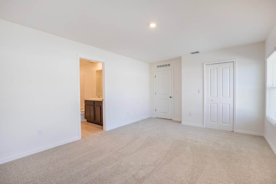 Empty, carpeted bedroom with white walls and a view into an adjacent bathroom.