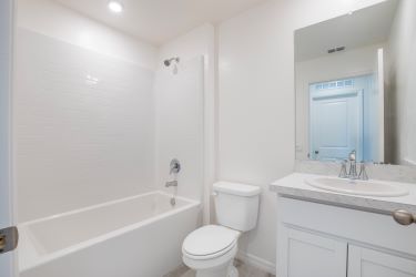 Modern white bathroom interior with bathtub, toilet, and sink featuring a large mirror.
